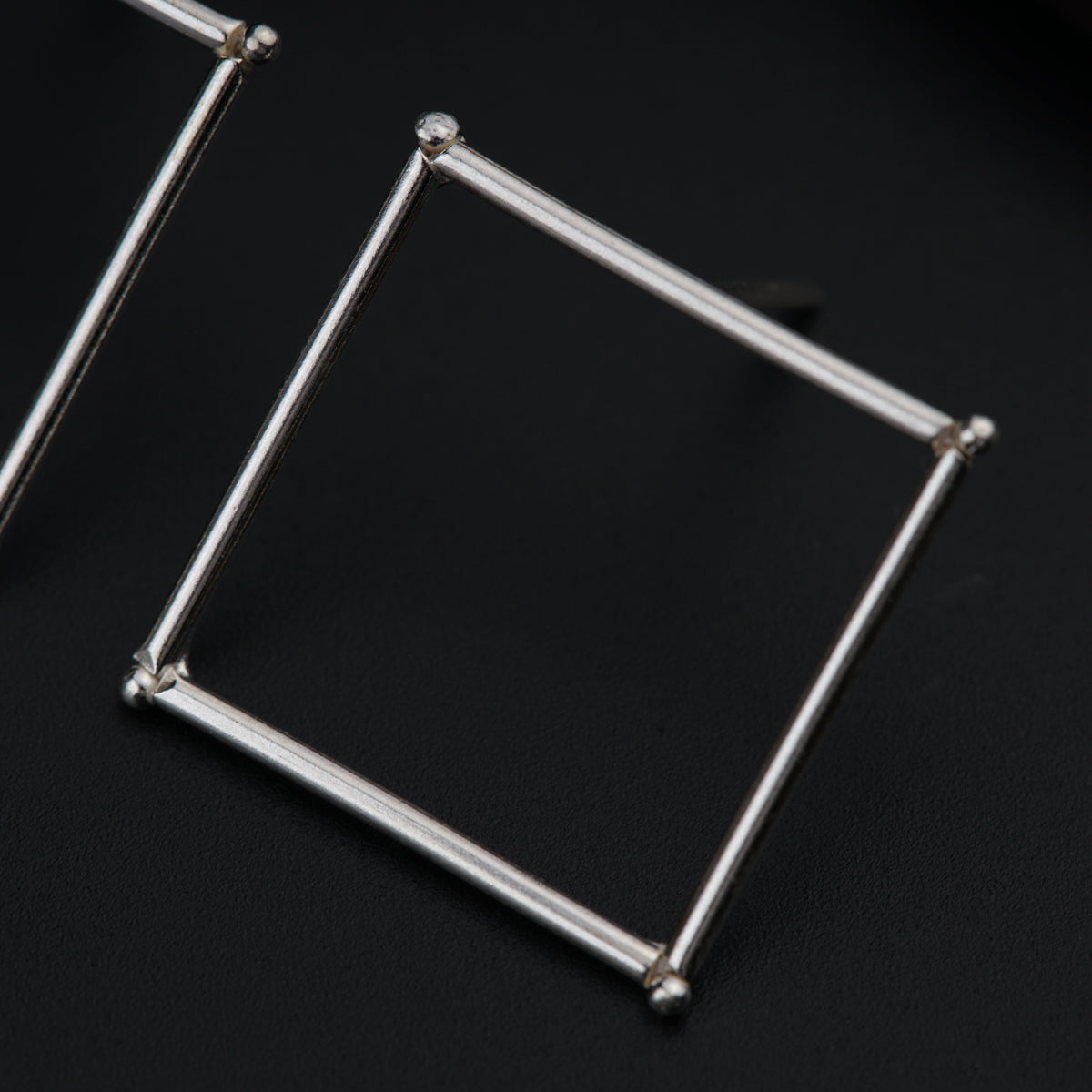 a pair of square silver earrings on a black surface