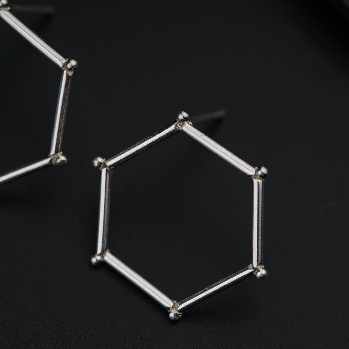 a pair of silver hexagonal earrings on a black surface