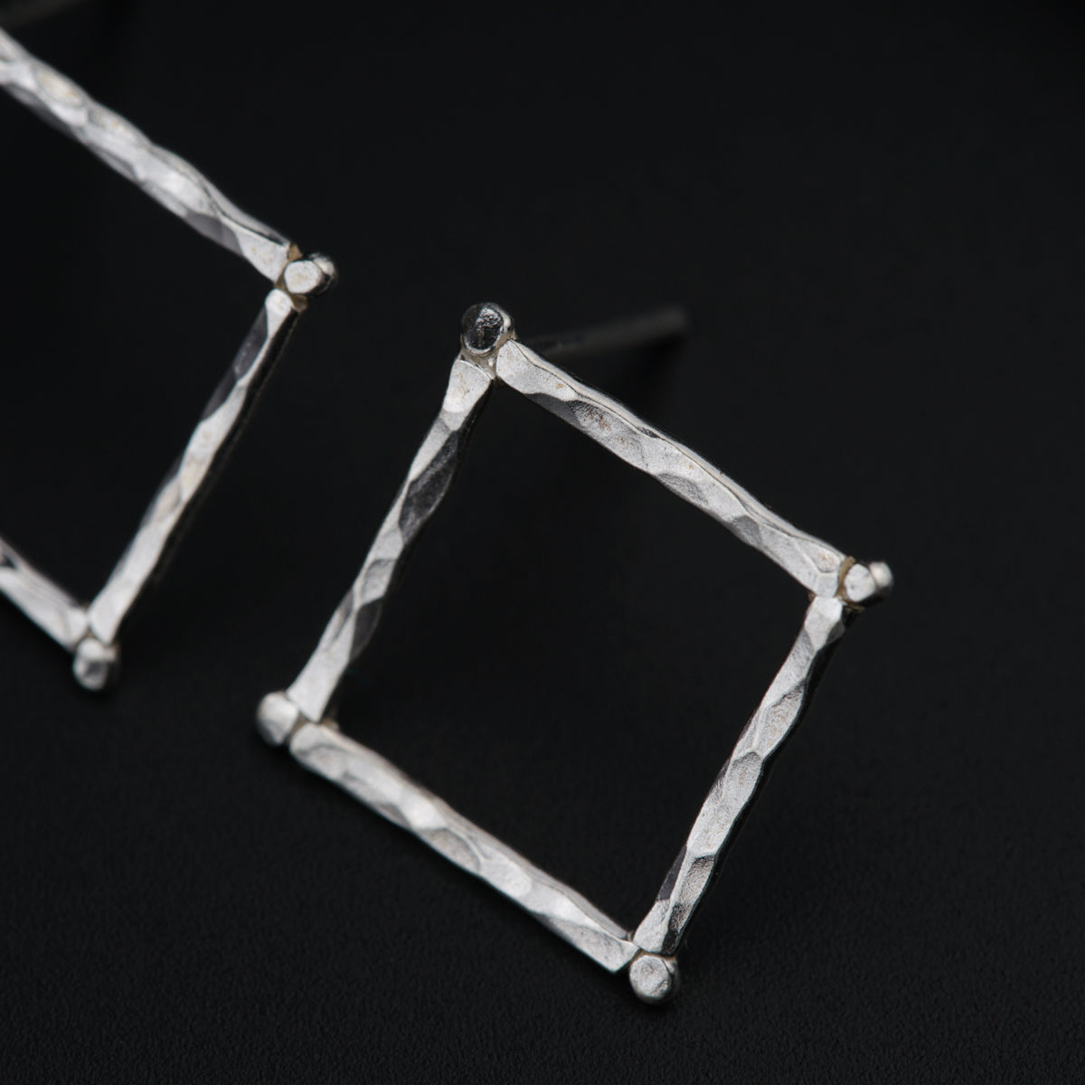 a pair of silver square earrings on a black background