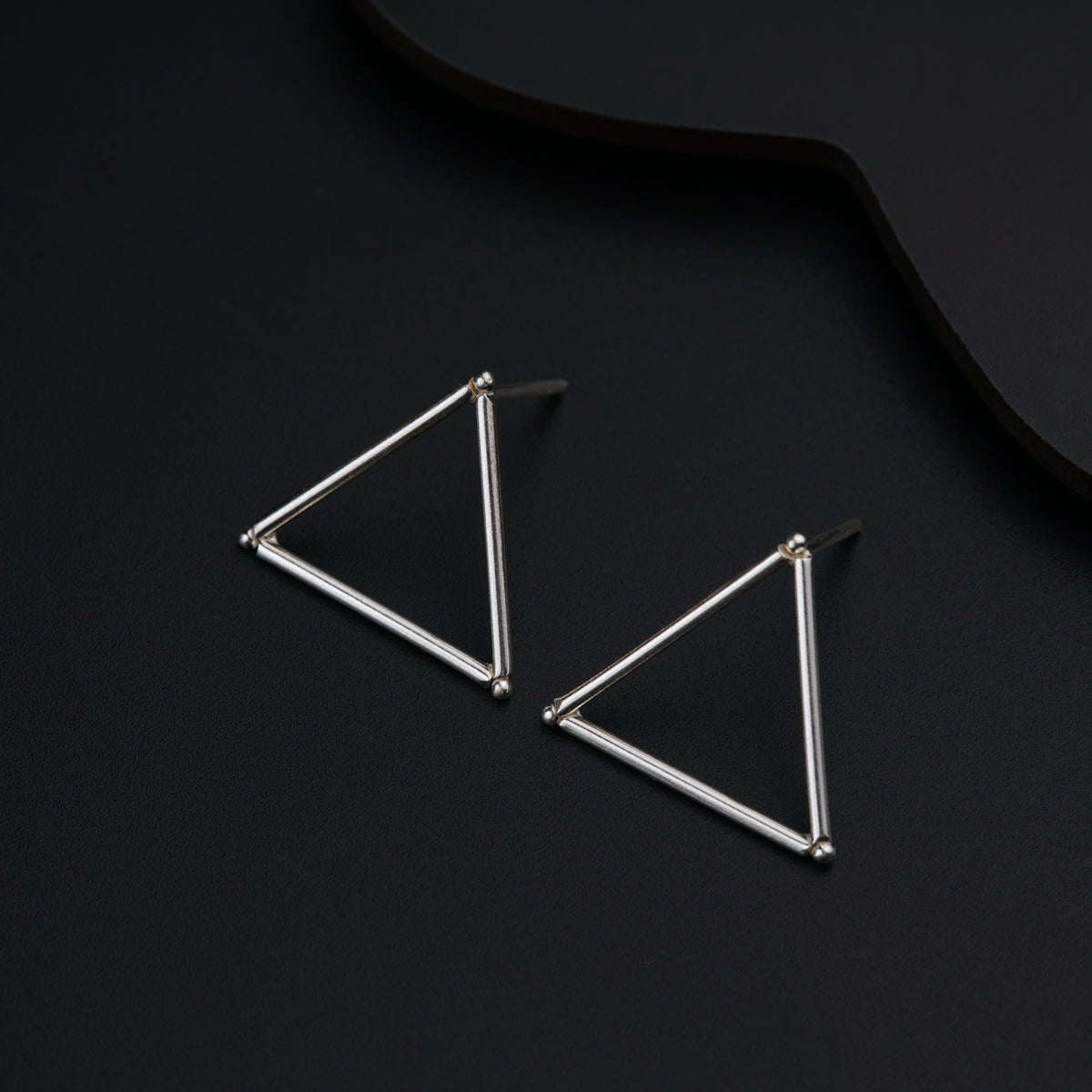 a pair of triangle earrings on a black surface