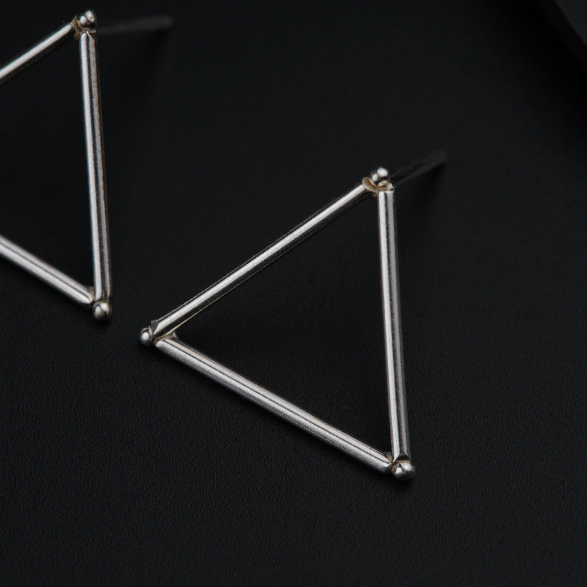 a pair of triangle earrings on a black surface