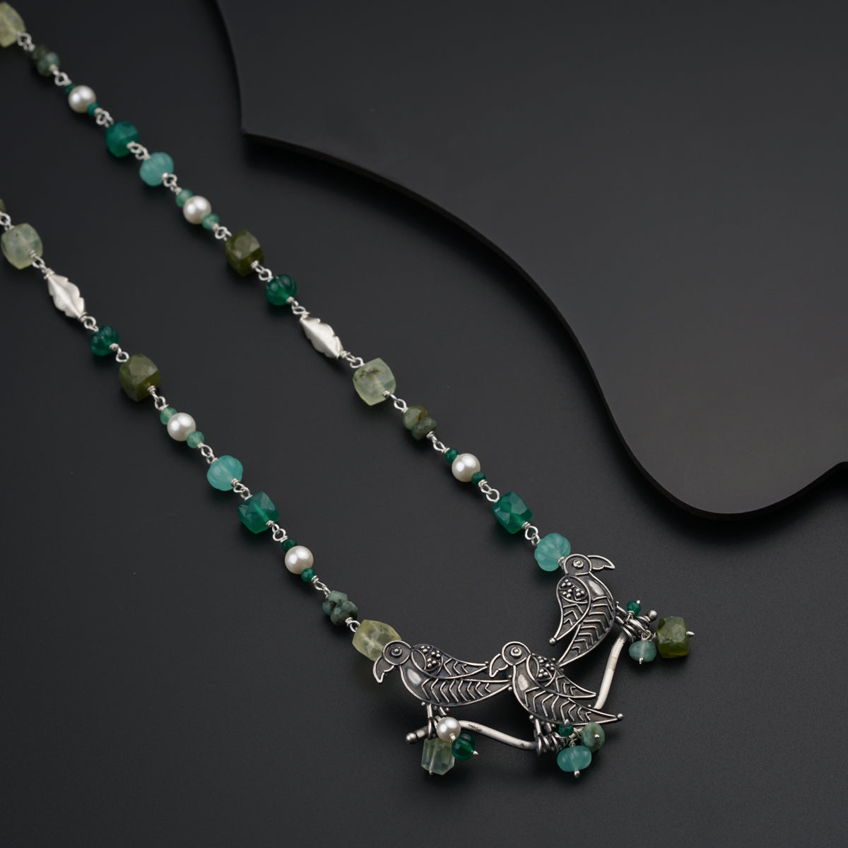 a necklace with green beads and a bird on it