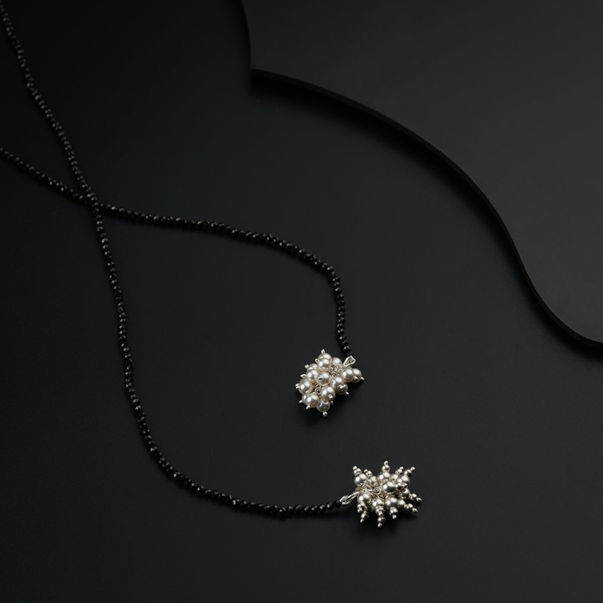 two necklaces with pearls on a black surface