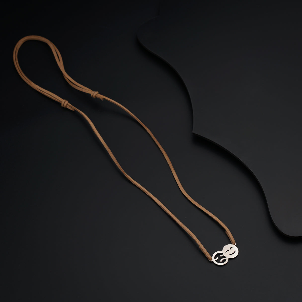 a brown cord with a silver pendant on a black background