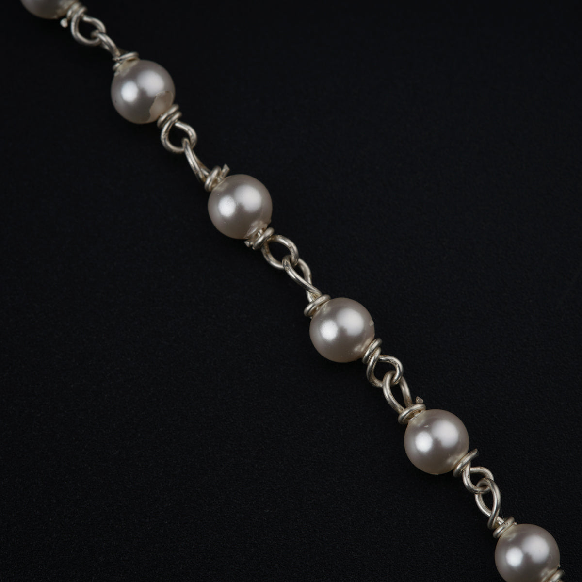 a silver bracelet with pearls on a black background
