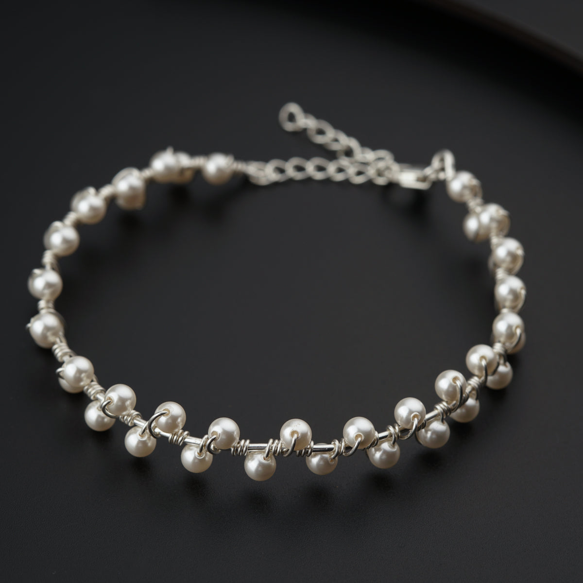 a silver bracelet with pearls on a black surface