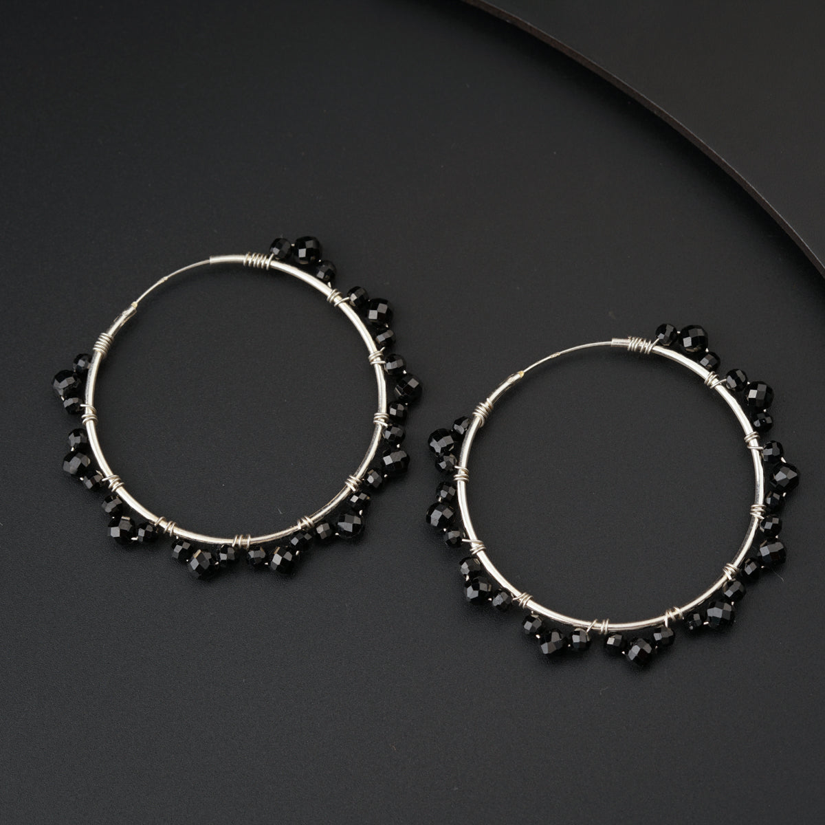 a pair of black beaded hoop earrings on a black surface
