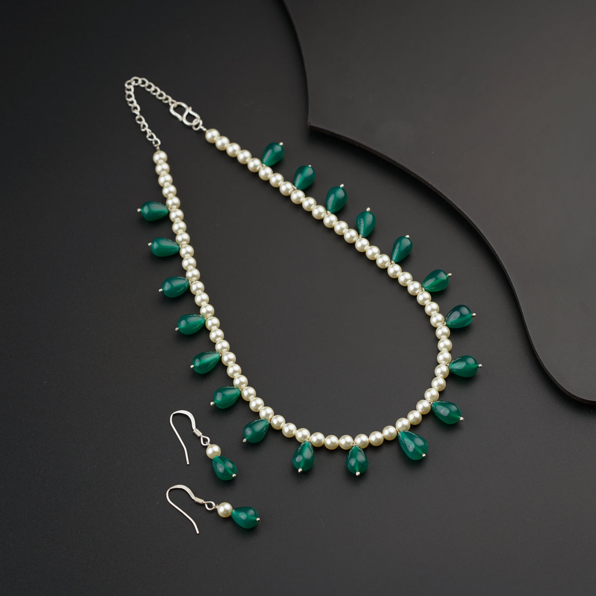 a green and white necklace and earrings on a black surface