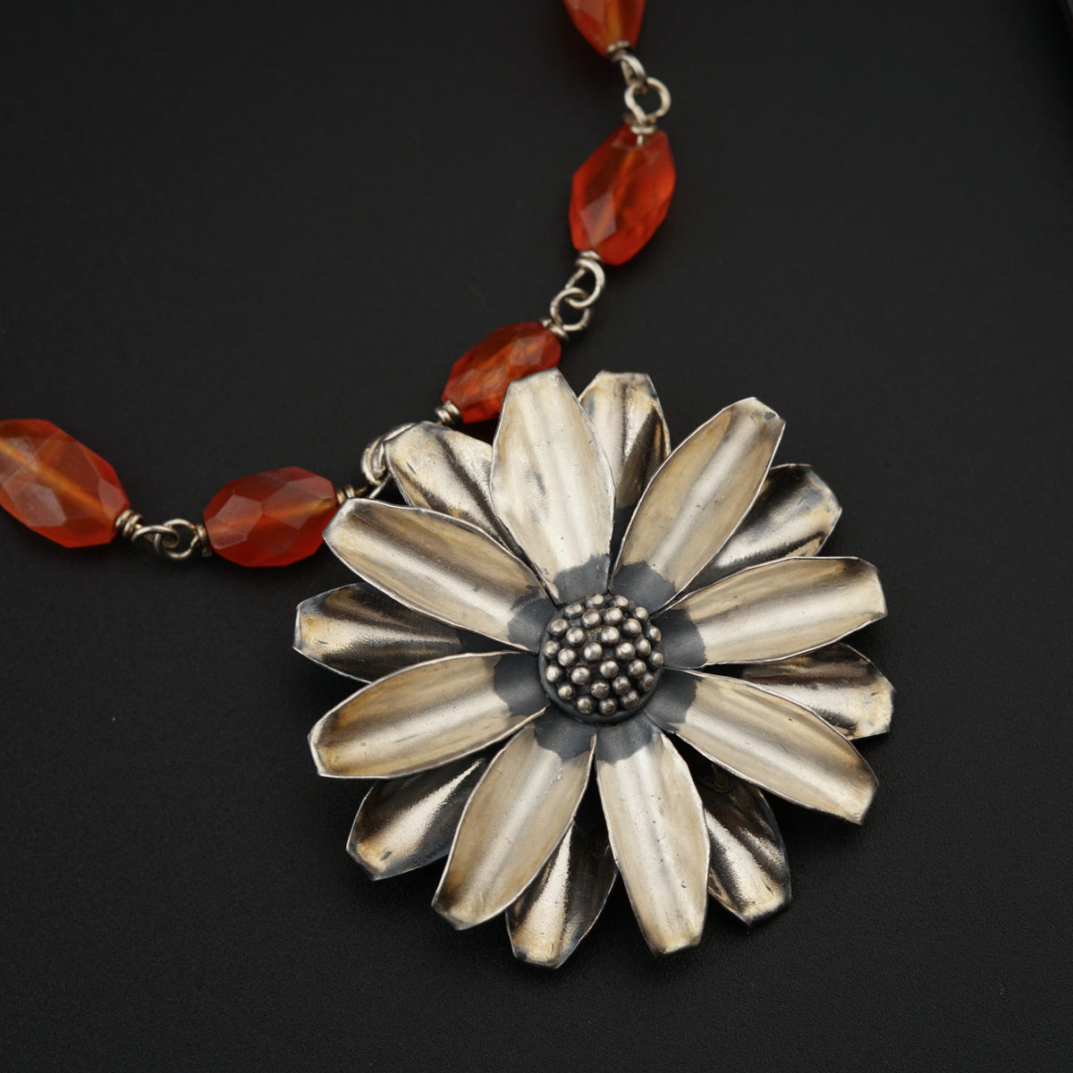 a necklace with a flower and beads on a black surface