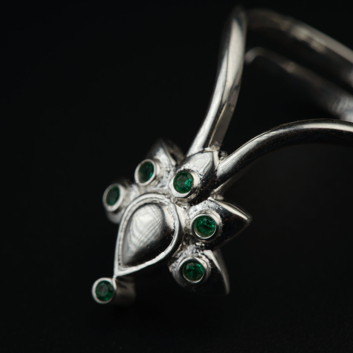 a close up of a silver ring with green stones