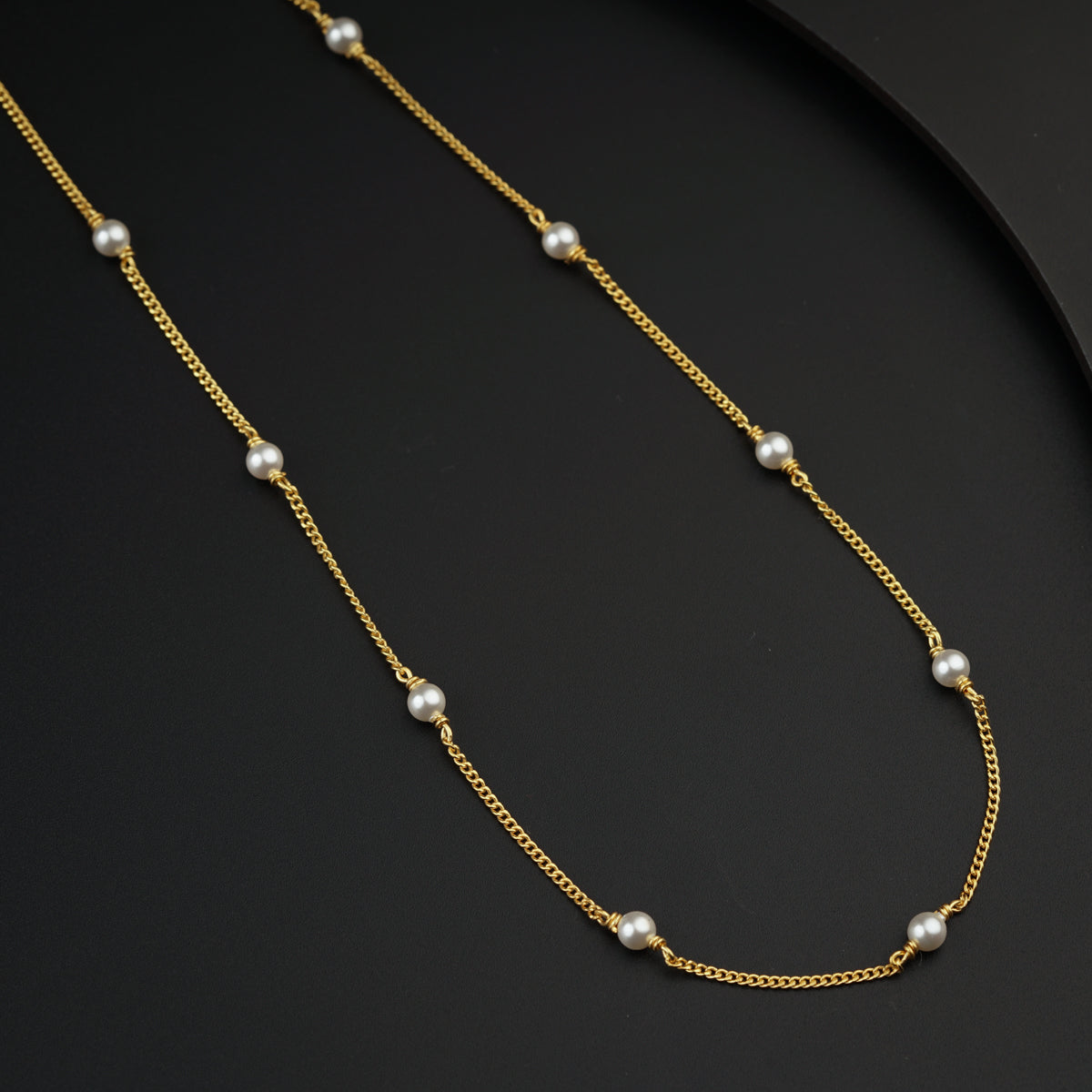 a gold necklace with pearls on a black surface