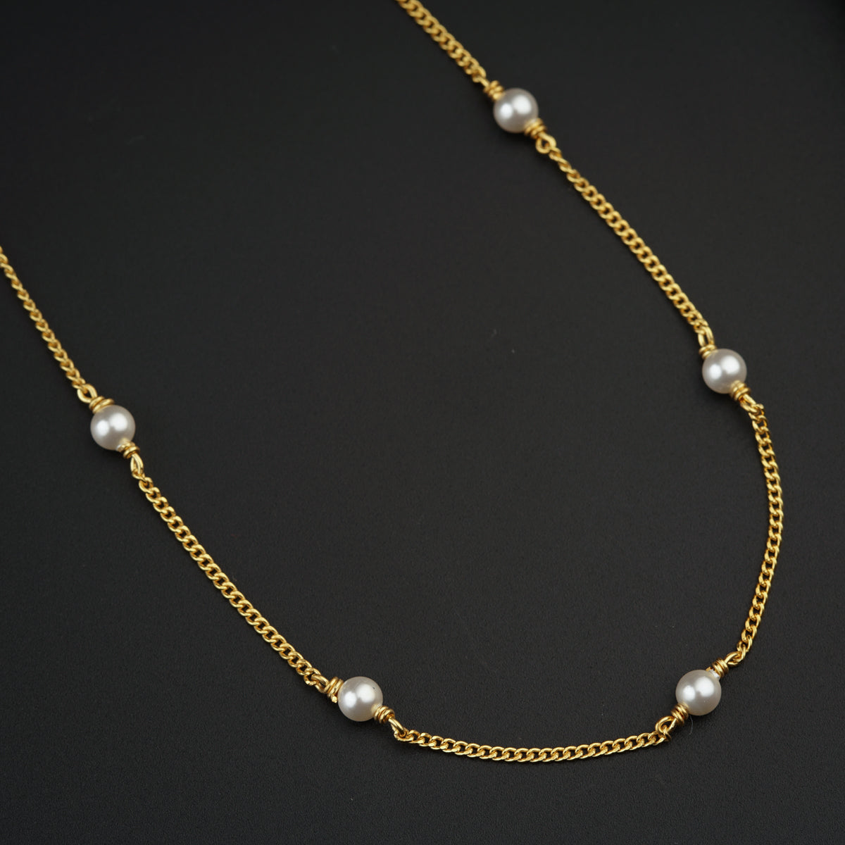 a gold necklace with pearls on a black surface