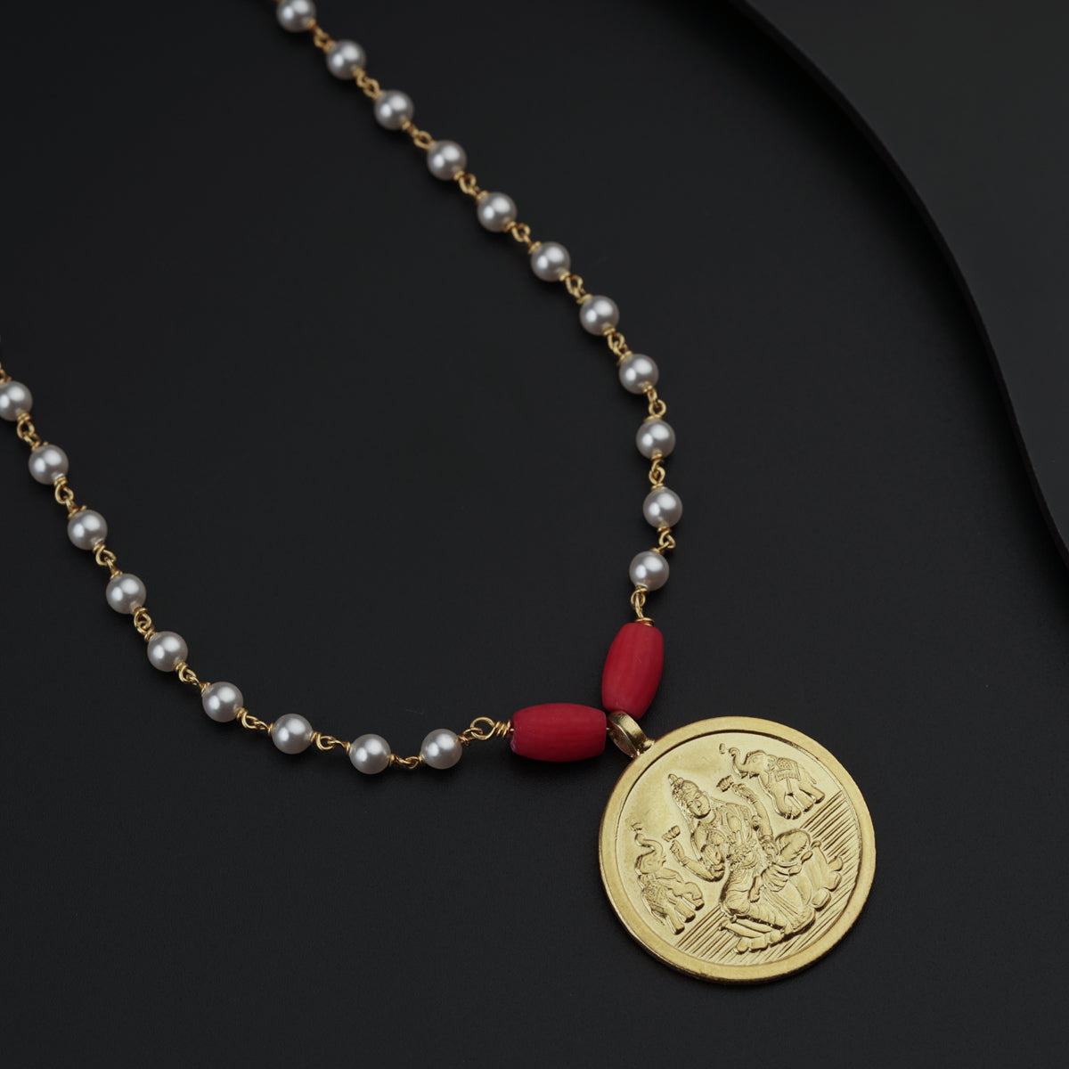 a necklace with a gold coin and a red bead