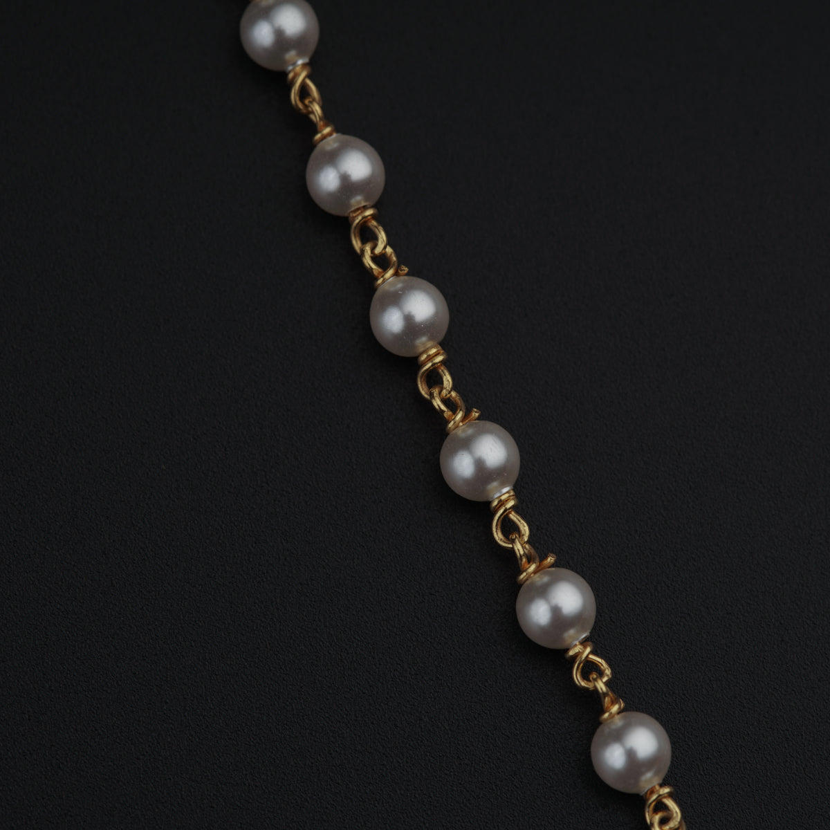 a bracelet with pearls and gold chains on a black surface