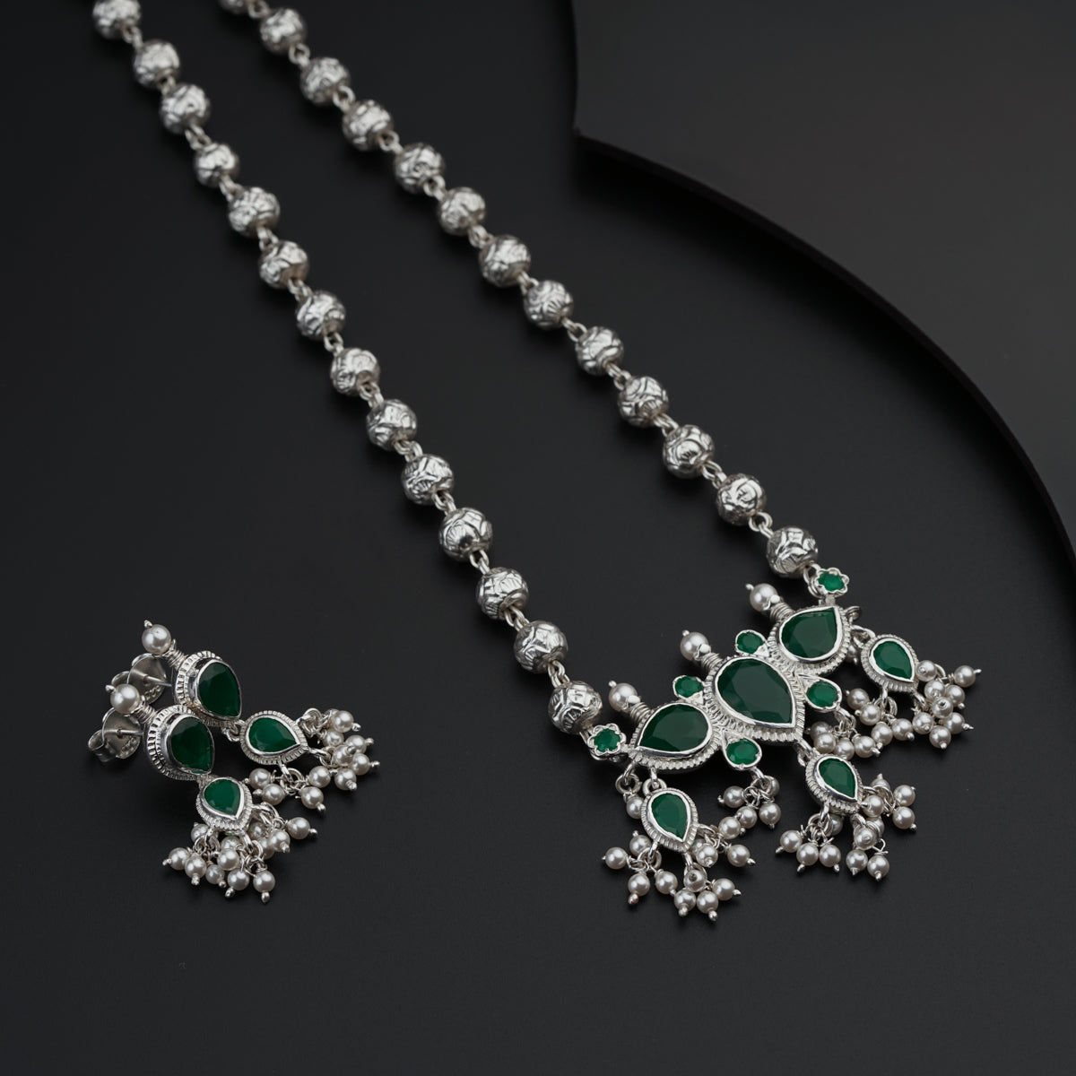 a green and white necklace and earrings on a black surface