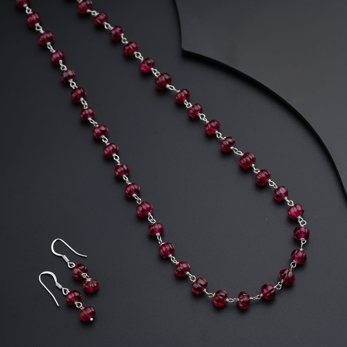 a red beaded necklace and earrings on a black surface