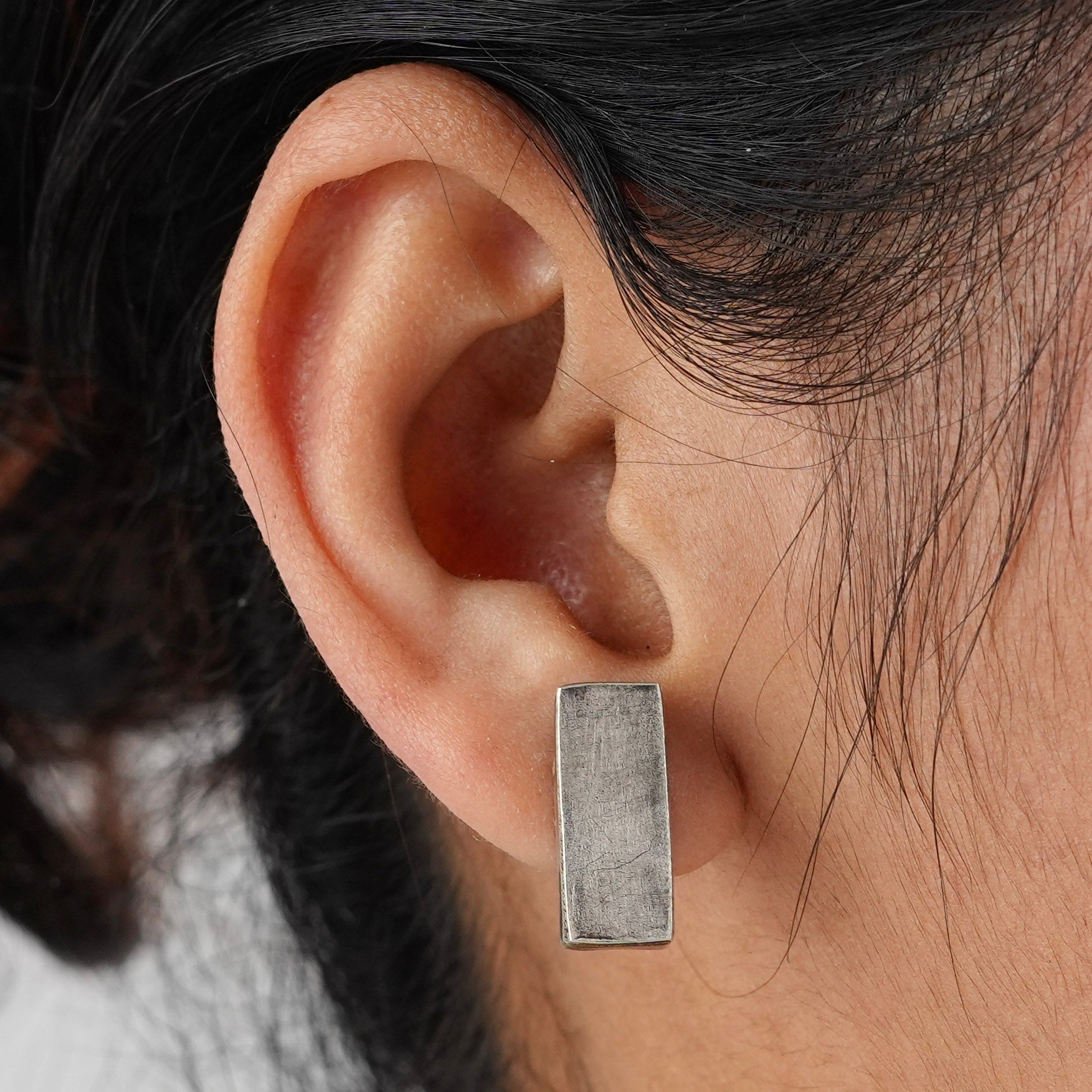 Silver rectangular earrings on ear