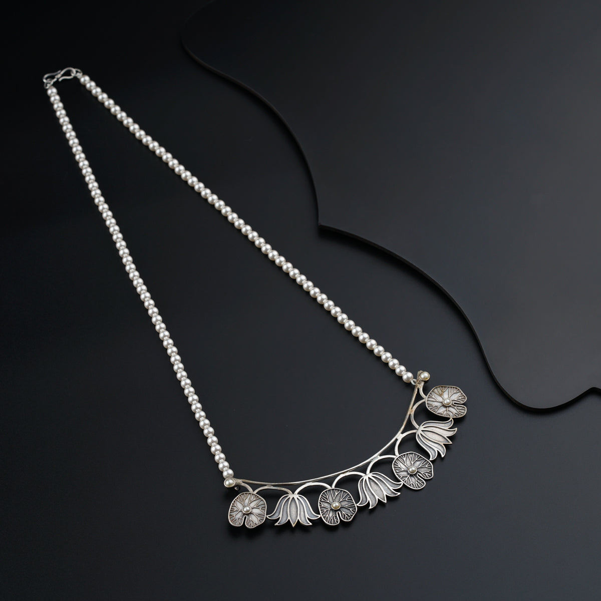 a silver necklace with flowers on a black background