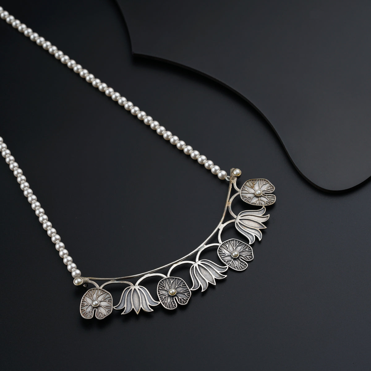 a silver necklace with flowers and leaves on a black surface