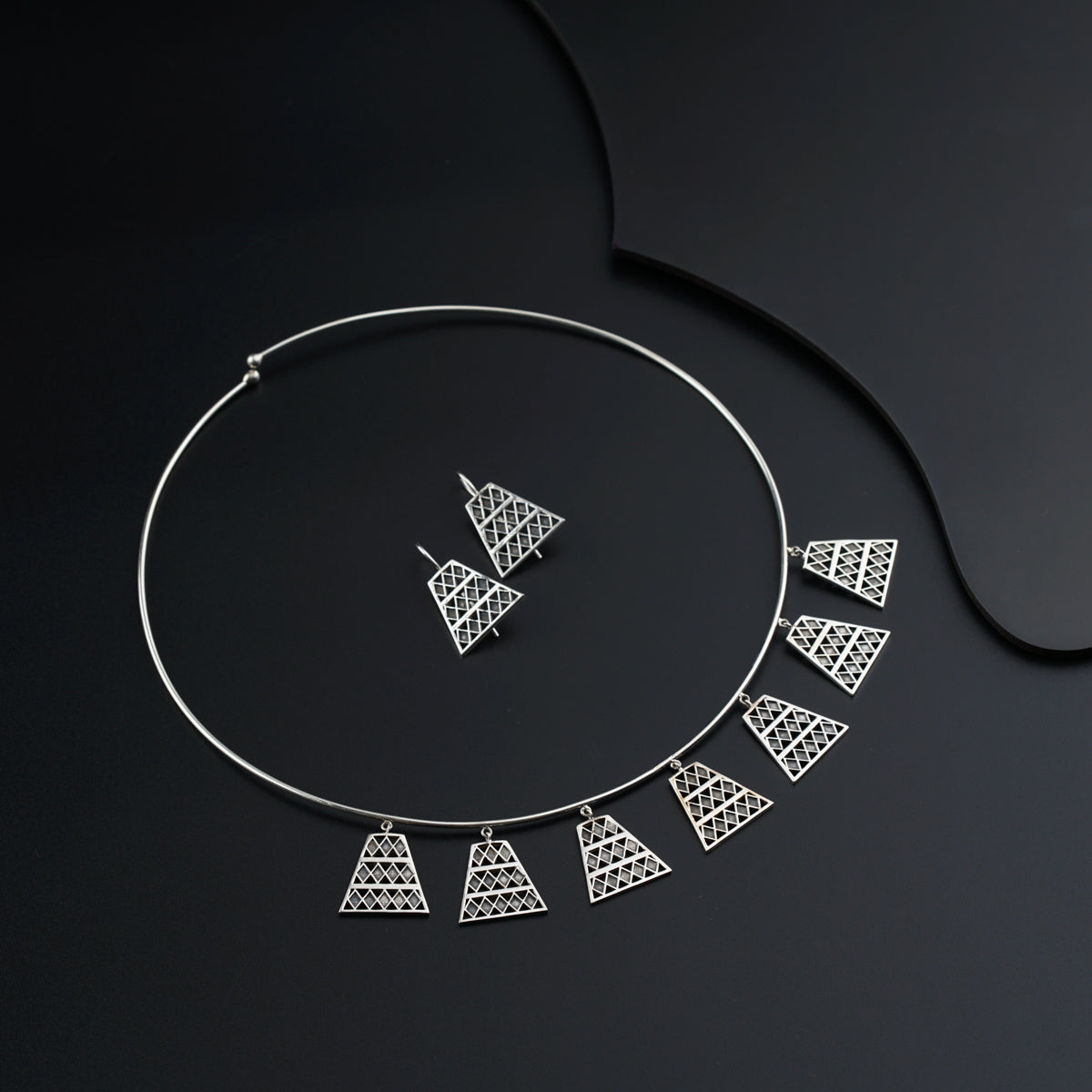 a silver necklace and a pair of earrings on a black surface