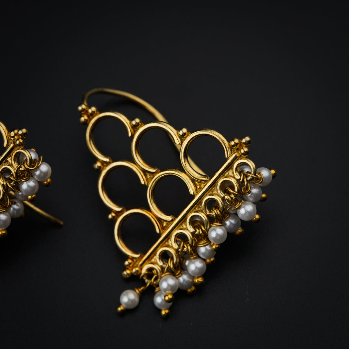 a pair of gold and pearl earrings on a black surface
