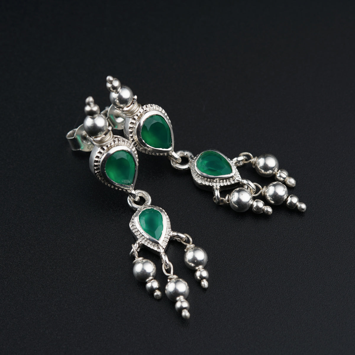a pair of green and silver earrings on a black surface