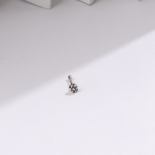 Silver nose pin with floral design on white surface