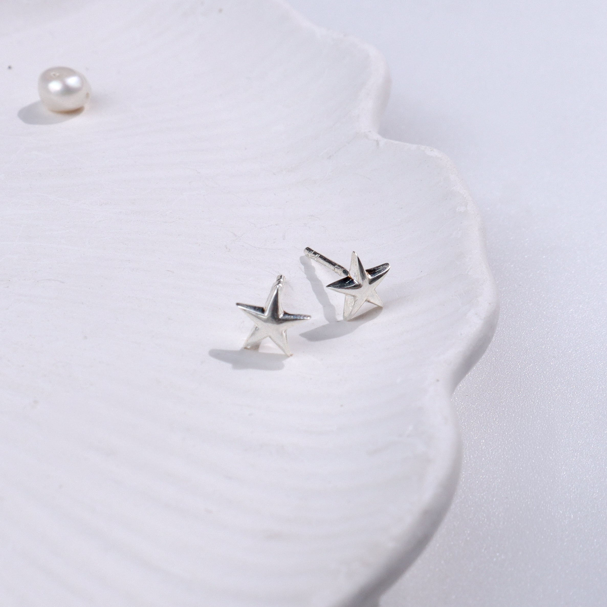 Silver starfish stud earrings on white textured surface