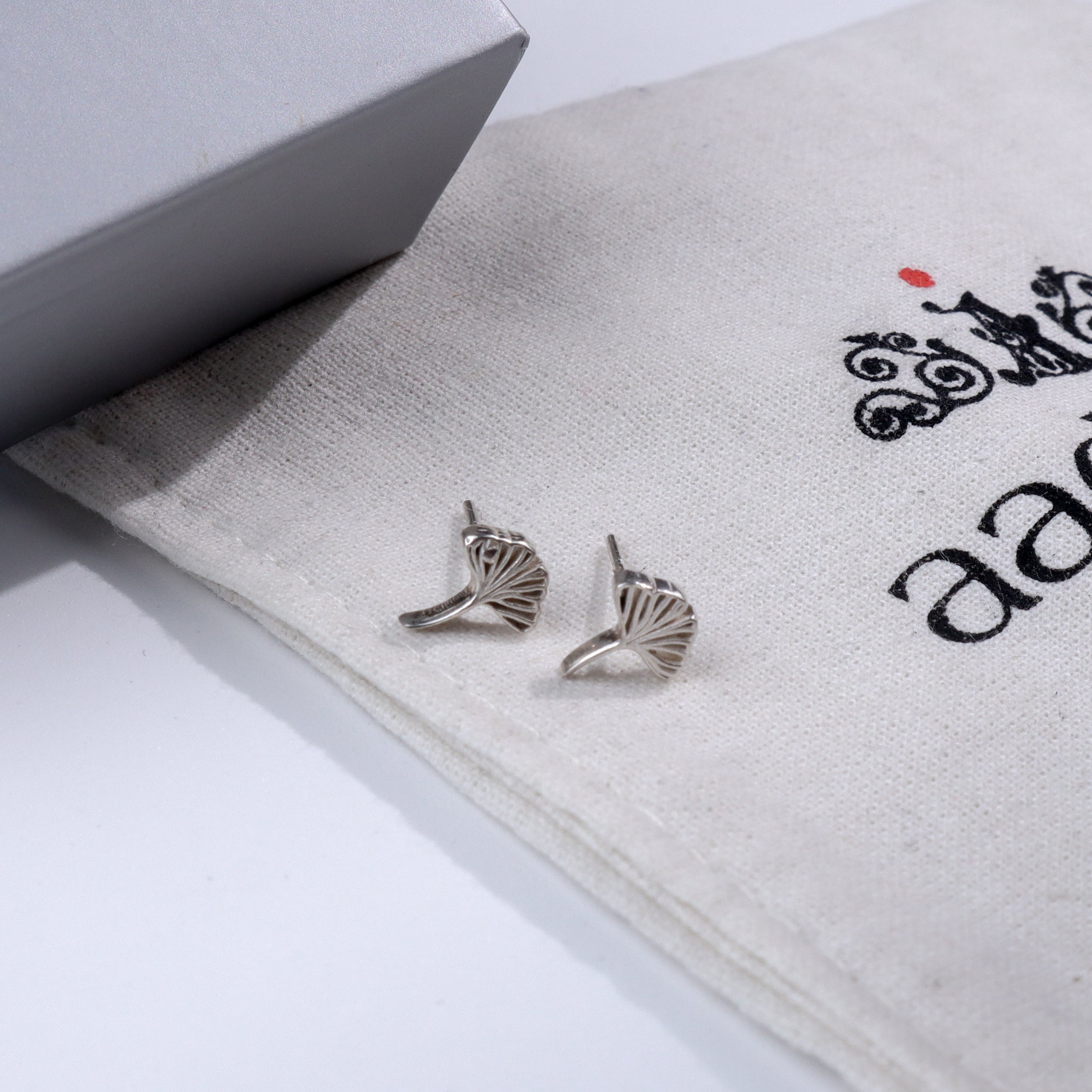 Silver Ginkgo Leaf Stud earrings on fabric with Aadyaa logo