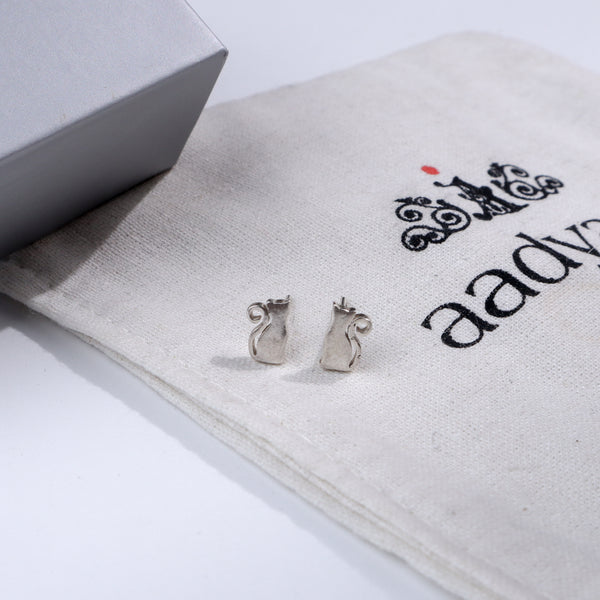 Silver cat stud earrings on fabric with Aadyaa logo