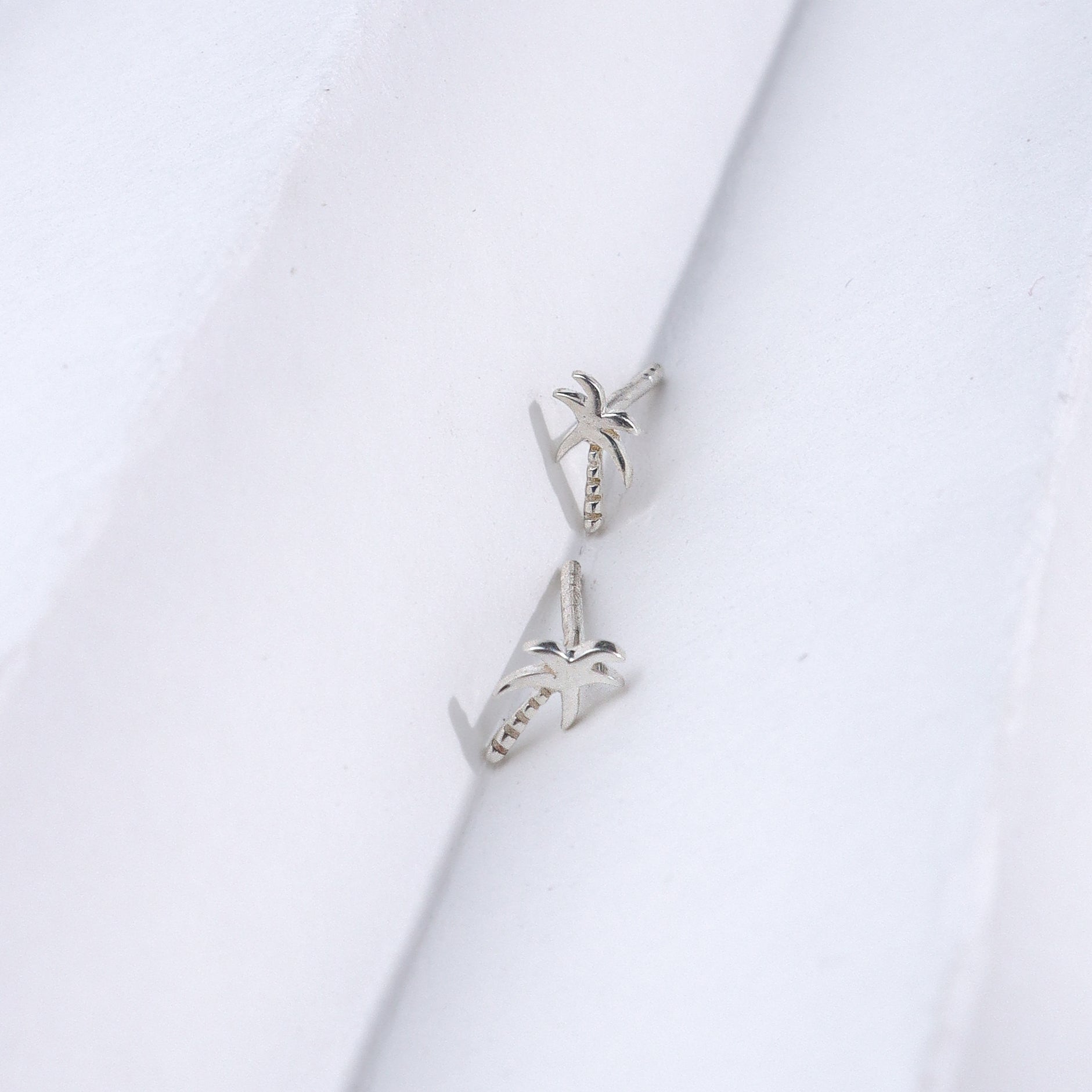 Silver coconut tree stud earrings on white background