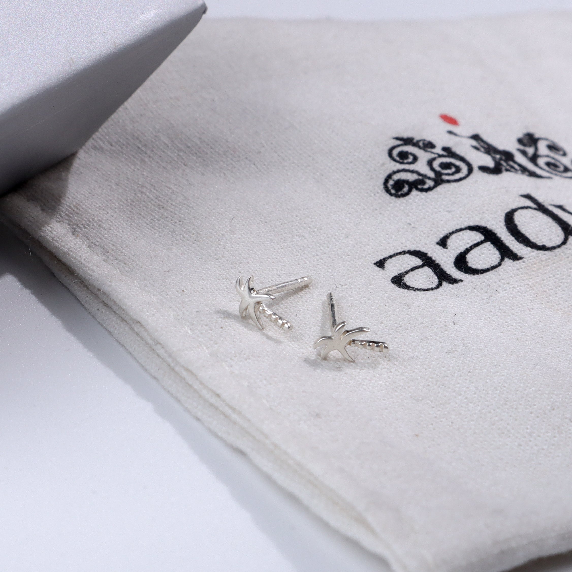 Silver palm tree stud earrings on fabric pouch