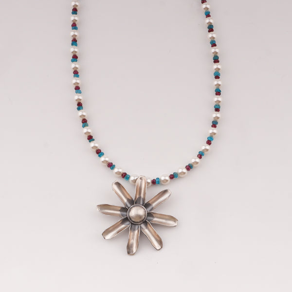 Close-up of beaded necklace with flower pendant, pearls, and stones