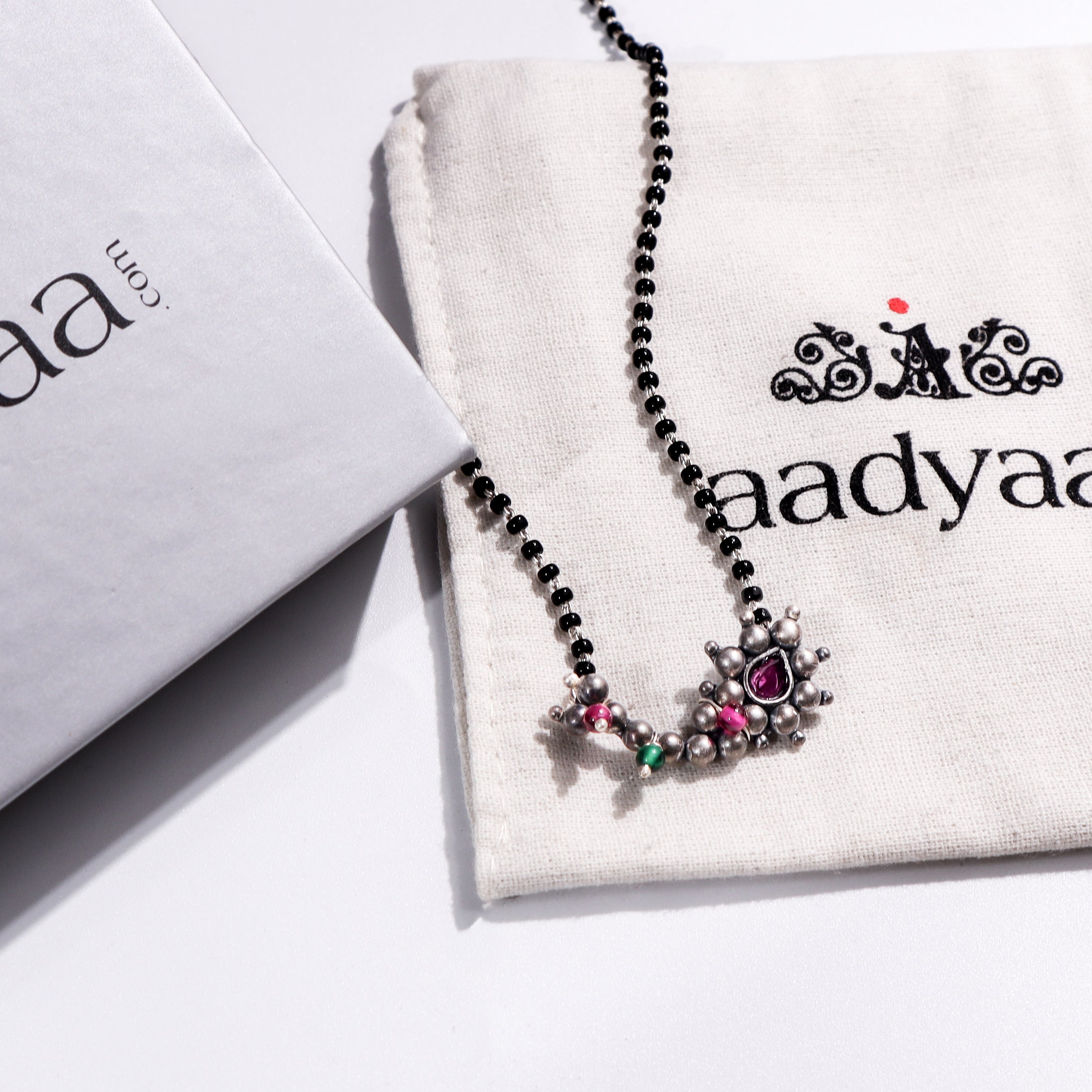 Maharashtrian silver mangalsutra with pink and green stones on Aadyaa jewelry pouch