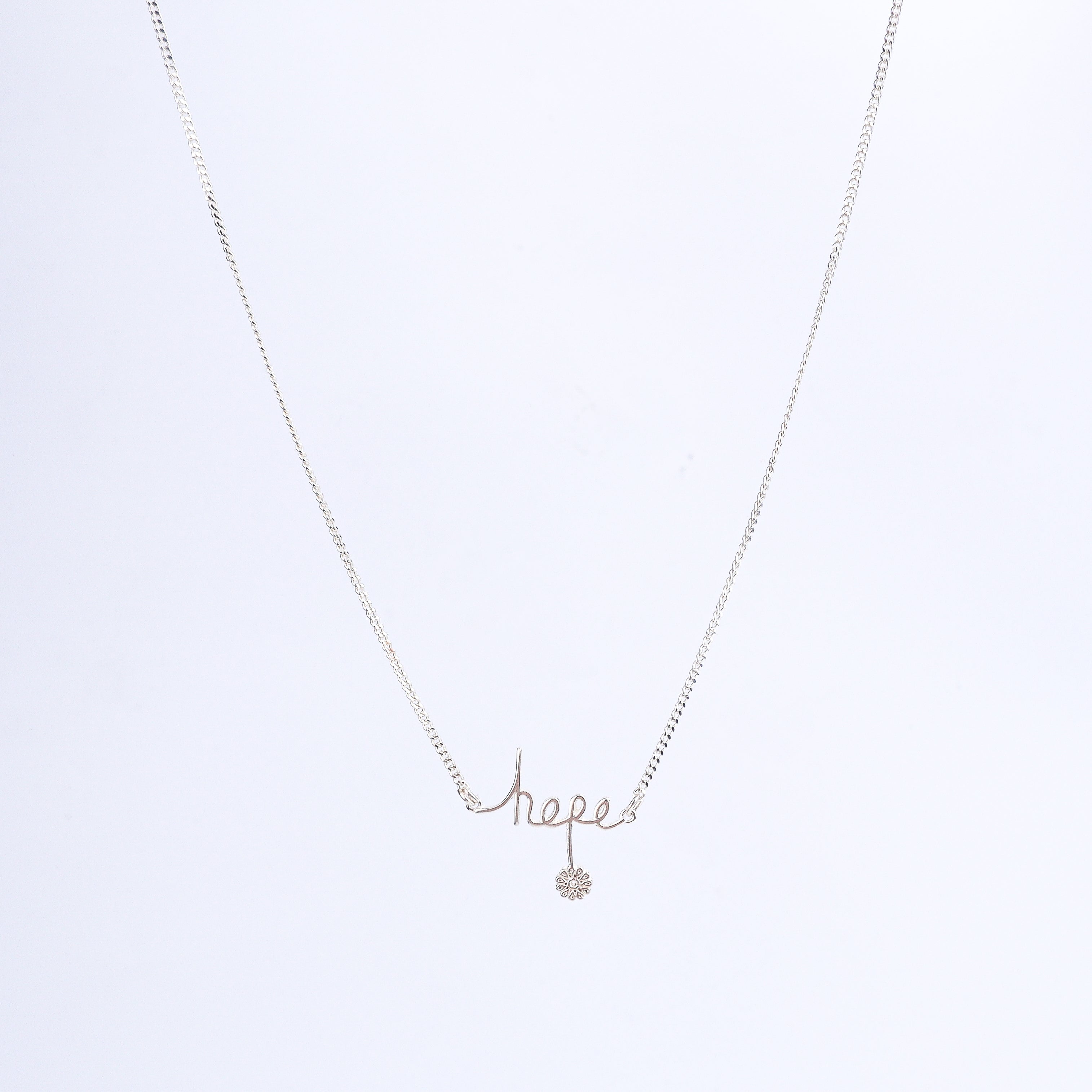 Flat-lay silver necklace with hope pendant on neutral background
