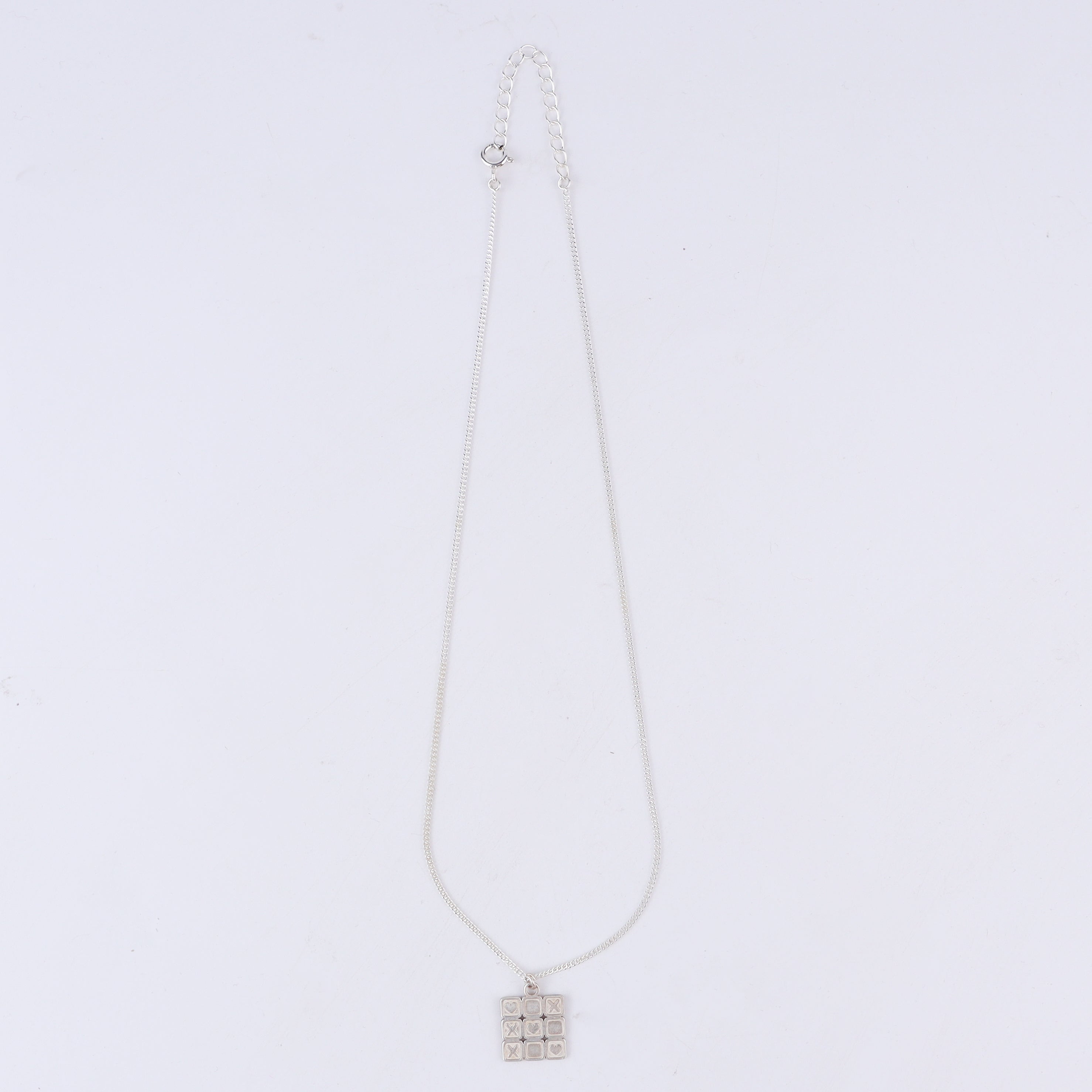 Close-up of tic tac toe grid detailing on big silver pendant