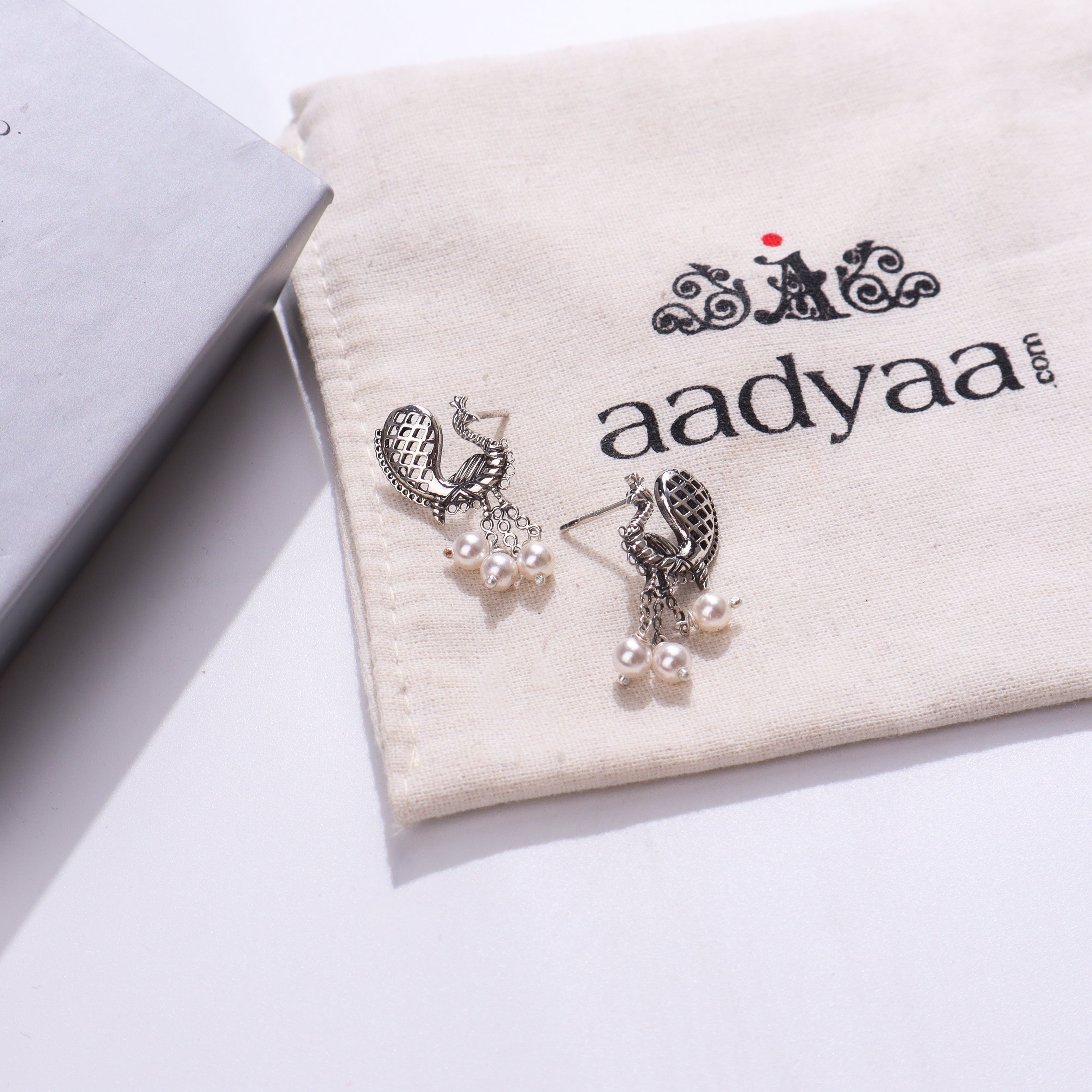 Silver peacock earrings with pearls on fabric pouch