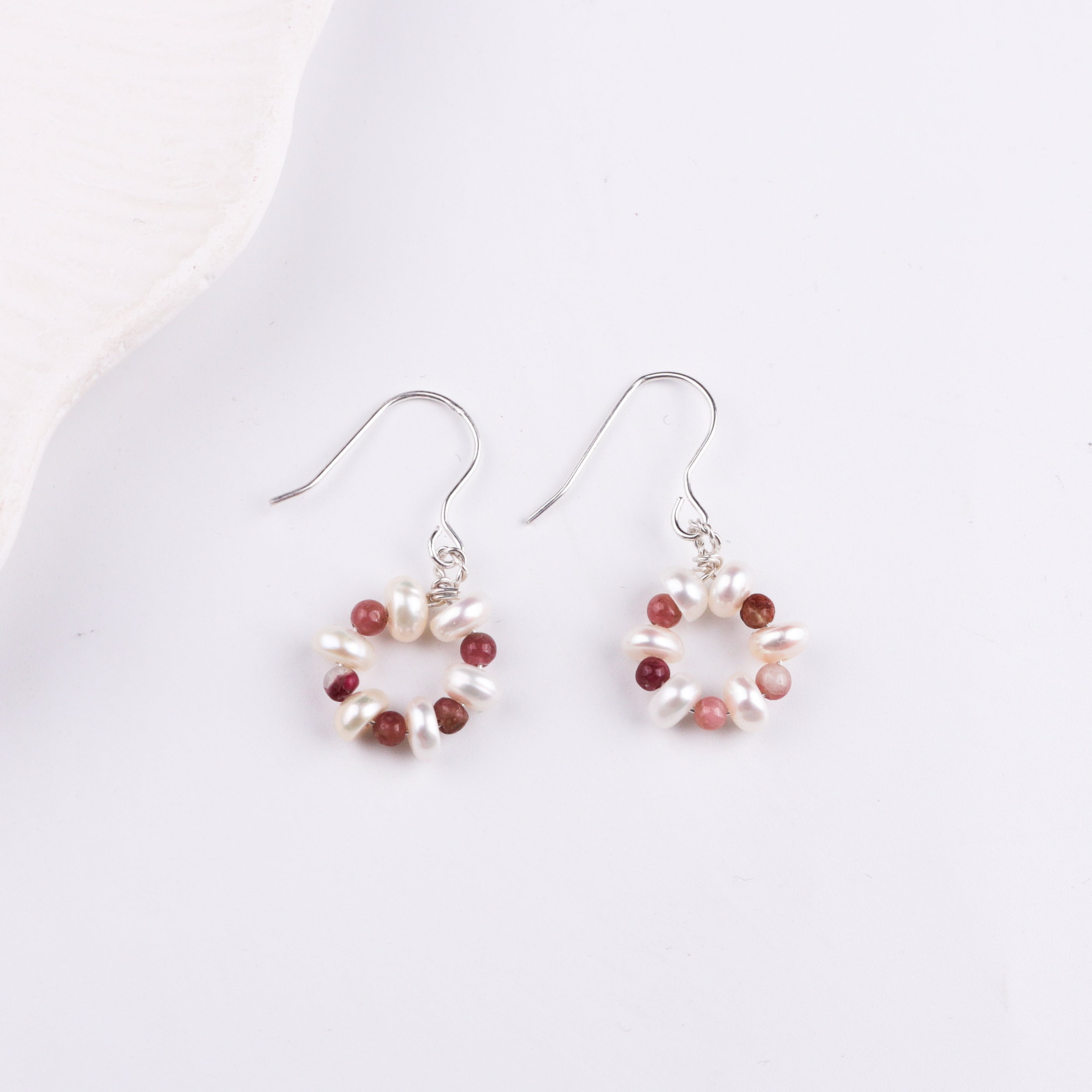 Pearl and red gemstone earrings on white surface