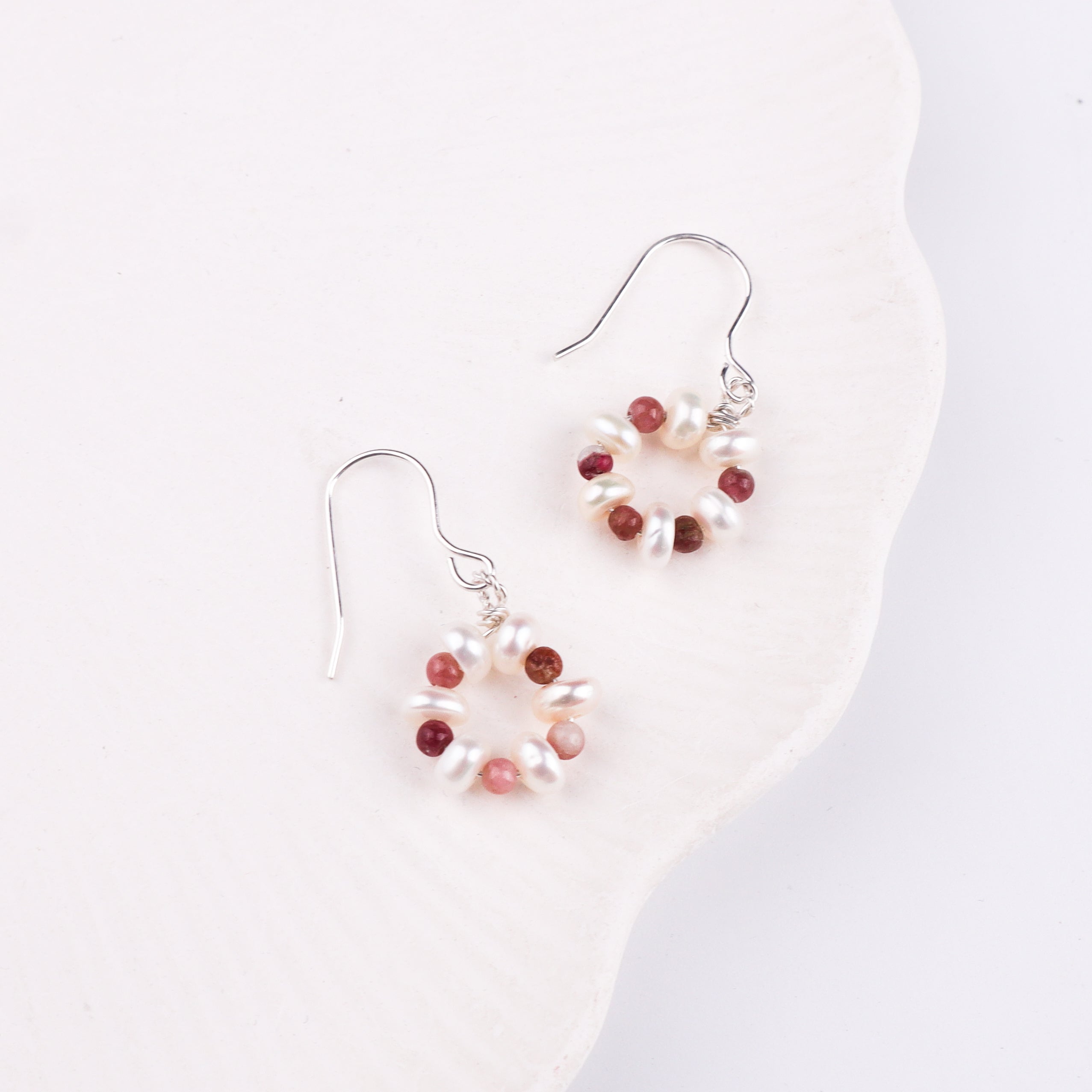 Silver earrings with pearls and red stones on white background