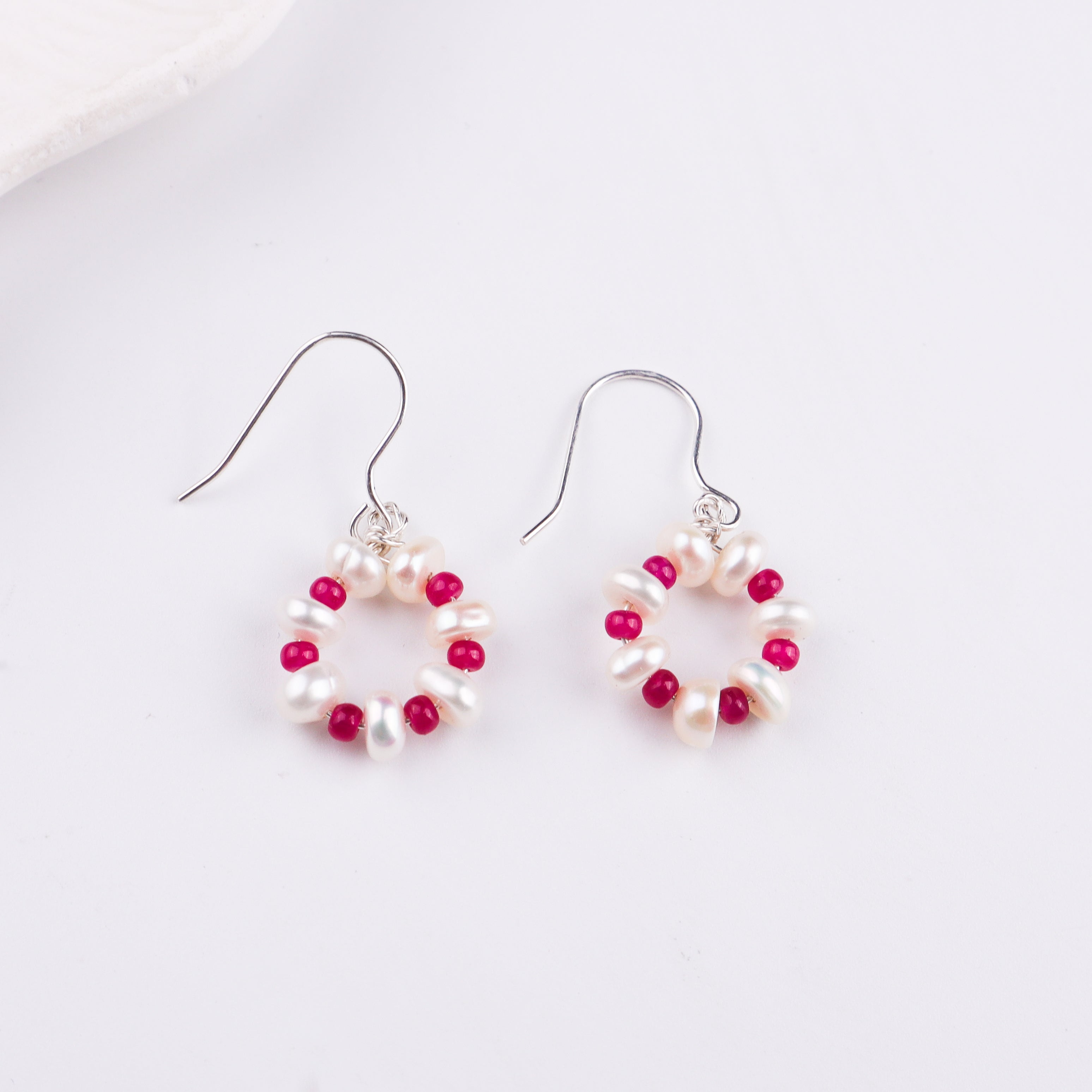 Pearl and ruby beaded earrings on white surface