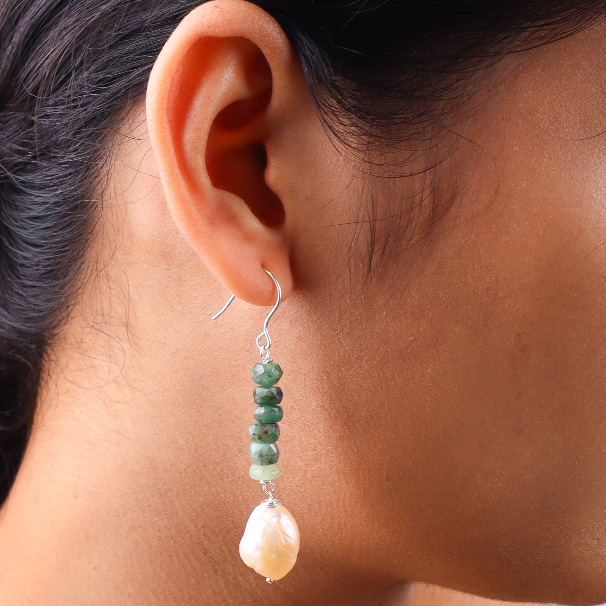 Close-up of silver hook earrings with green beads and pearl drops