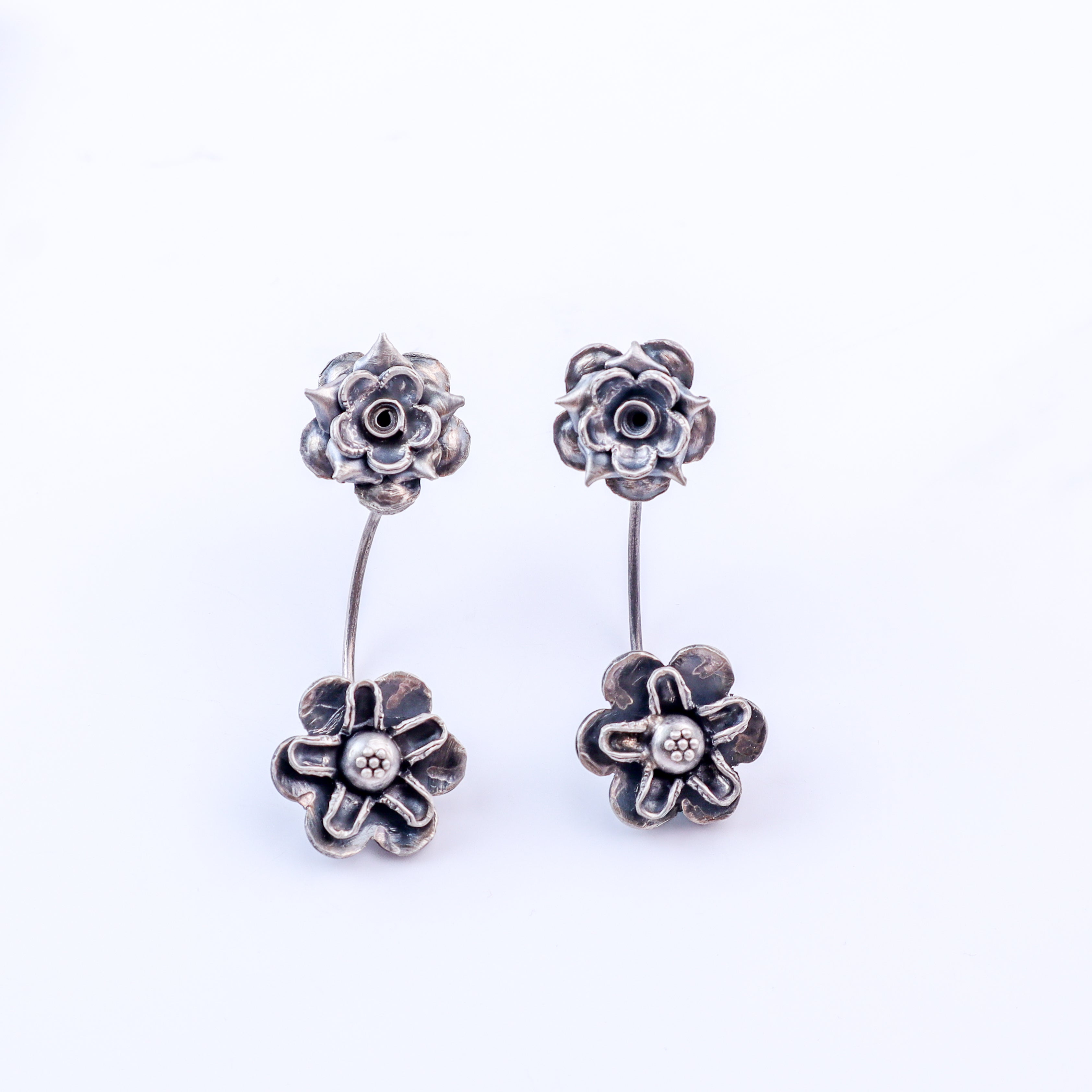 Flat-lay oxidized dual flower silver earrings on neutral background