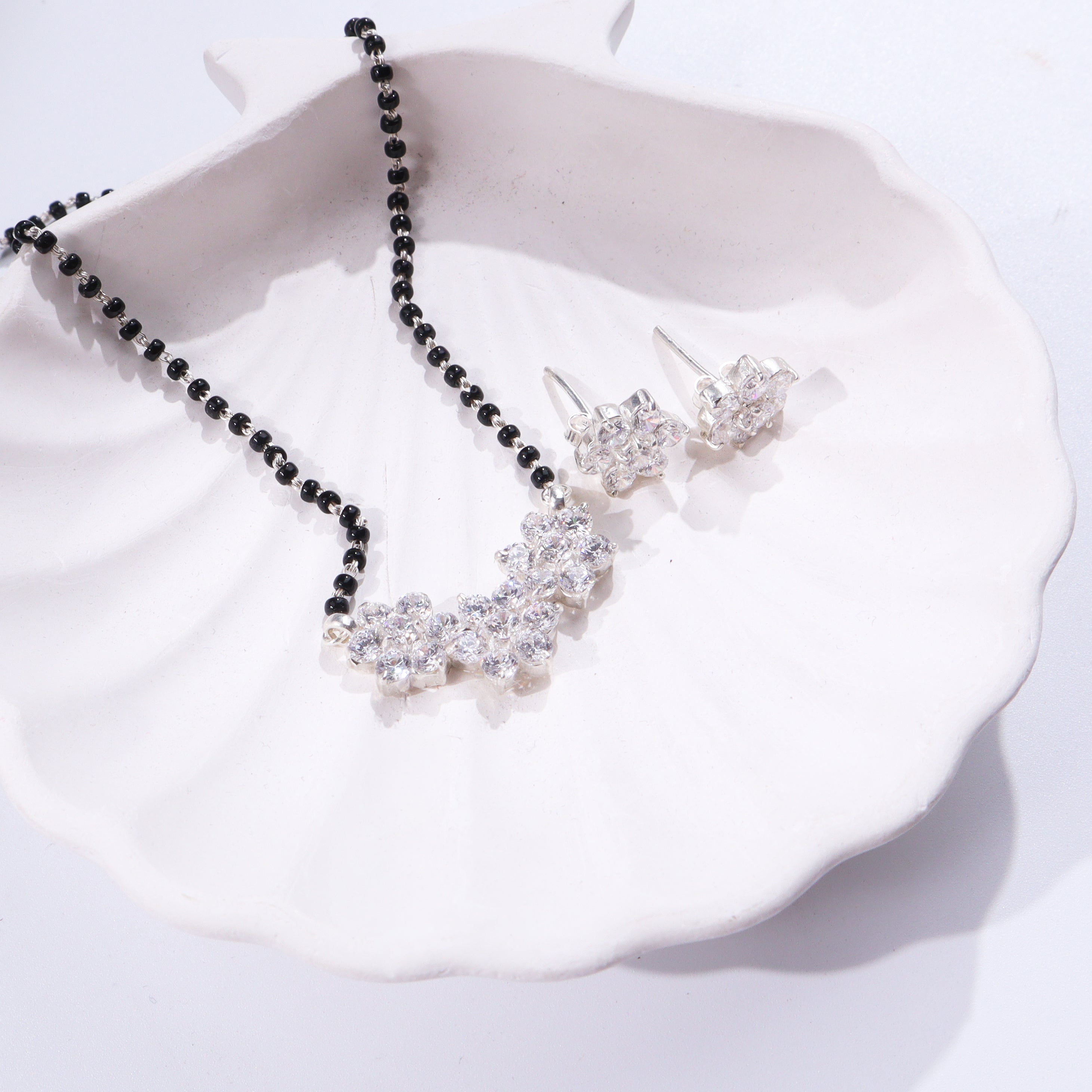 Black and silver beaded necklace with flower pendant on white ceramic dish