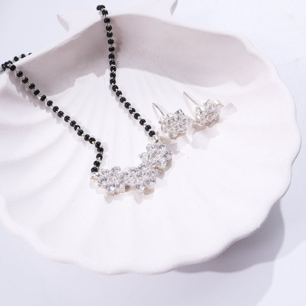 Black and silver beaded necklace with flower pendant on white ceramic dish