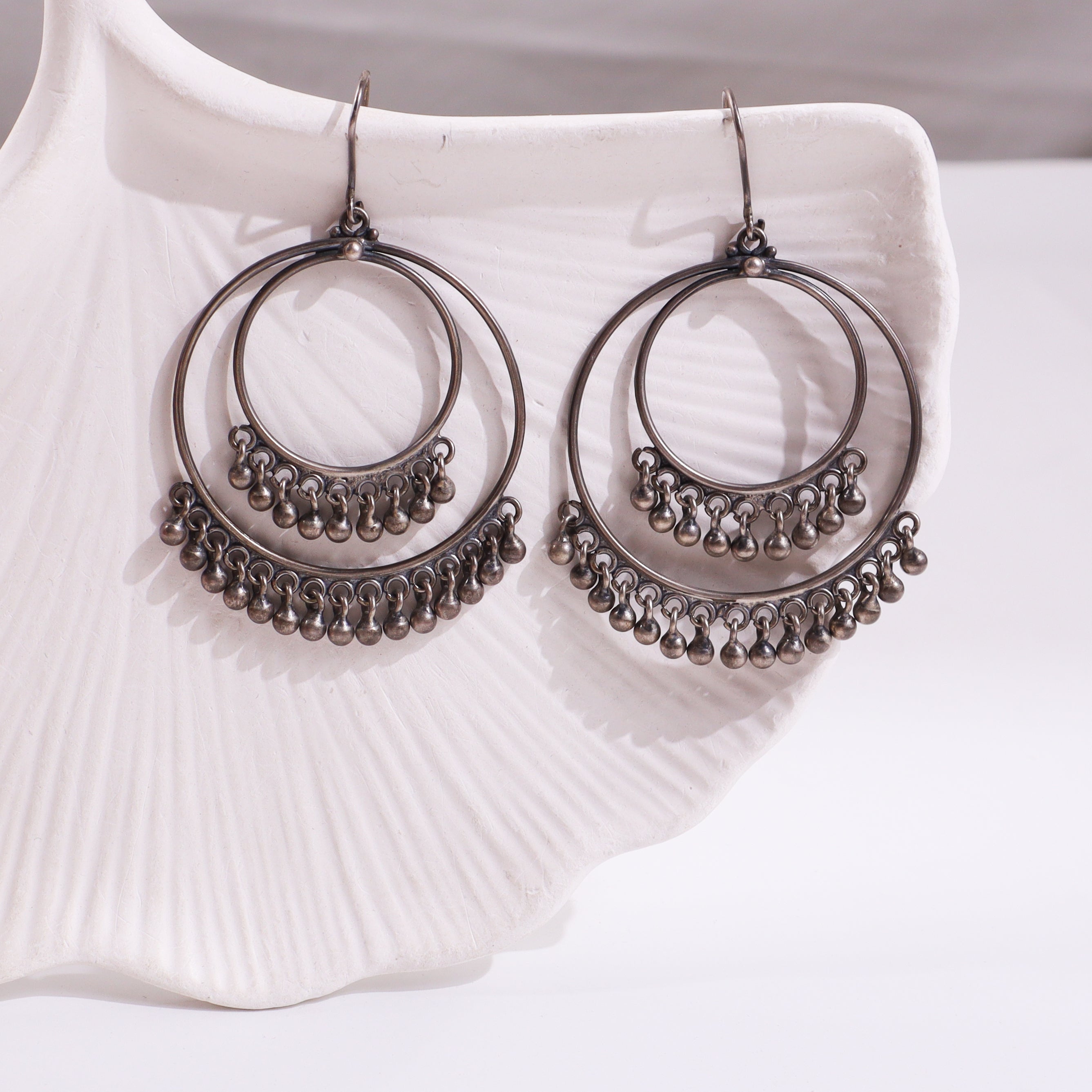 Silver hoop earrings with dangling beads on white ceramic dish