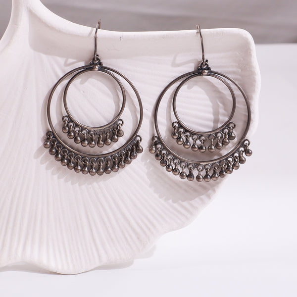 Silver hoop earrings with dangling beads on white ceramic dish