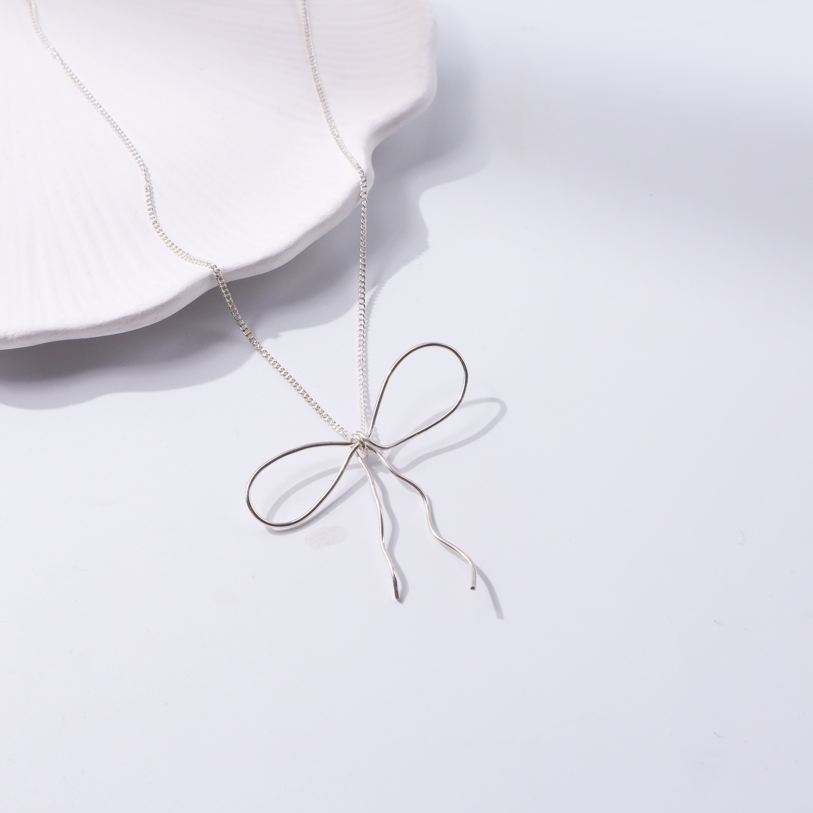 Silver bow necklace with delicate chain on white display