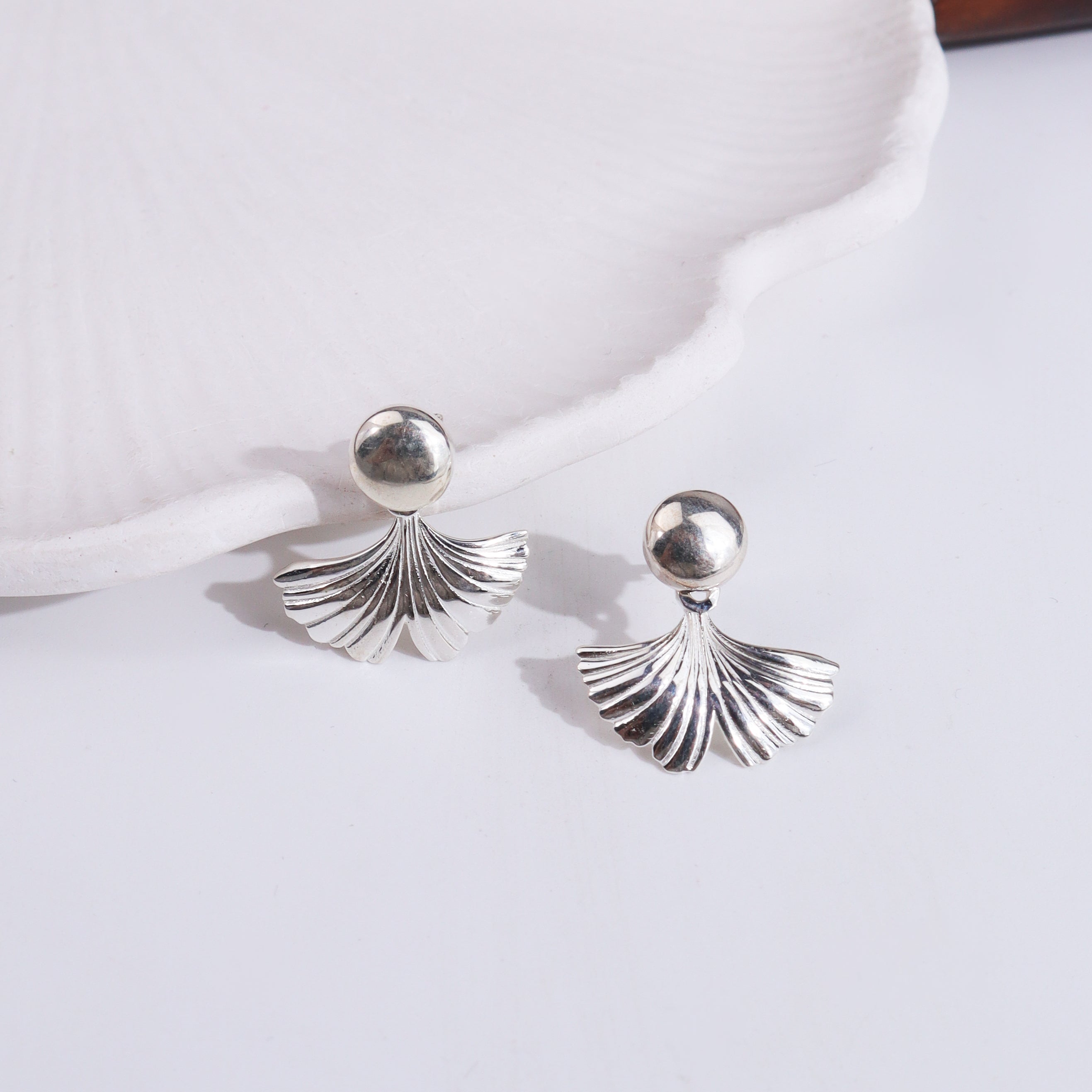 Silver earrings with ginkgo leaf motif on white surface