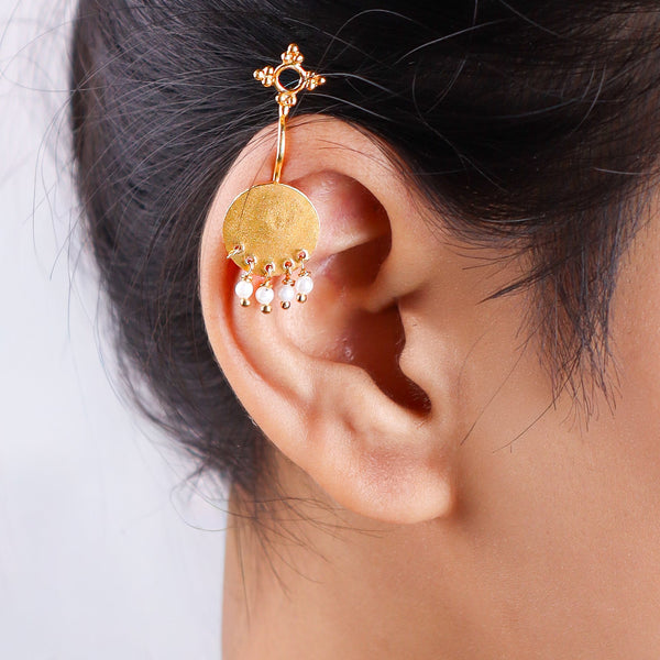 Gold earrings with circular pendant and pearl dangles worn on ear