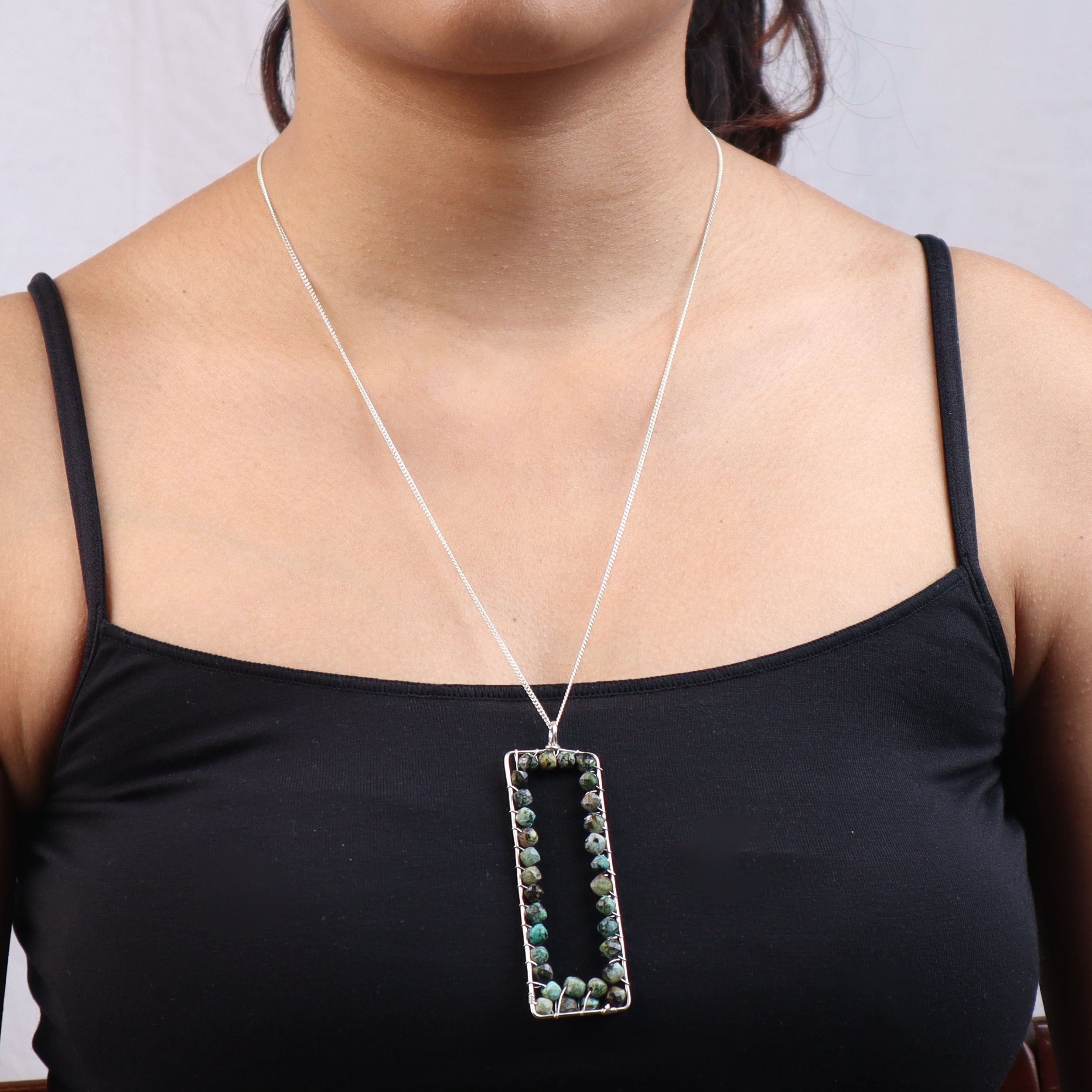 Silver necklace with rectangular pendant featuring green and black stones, worn with black top